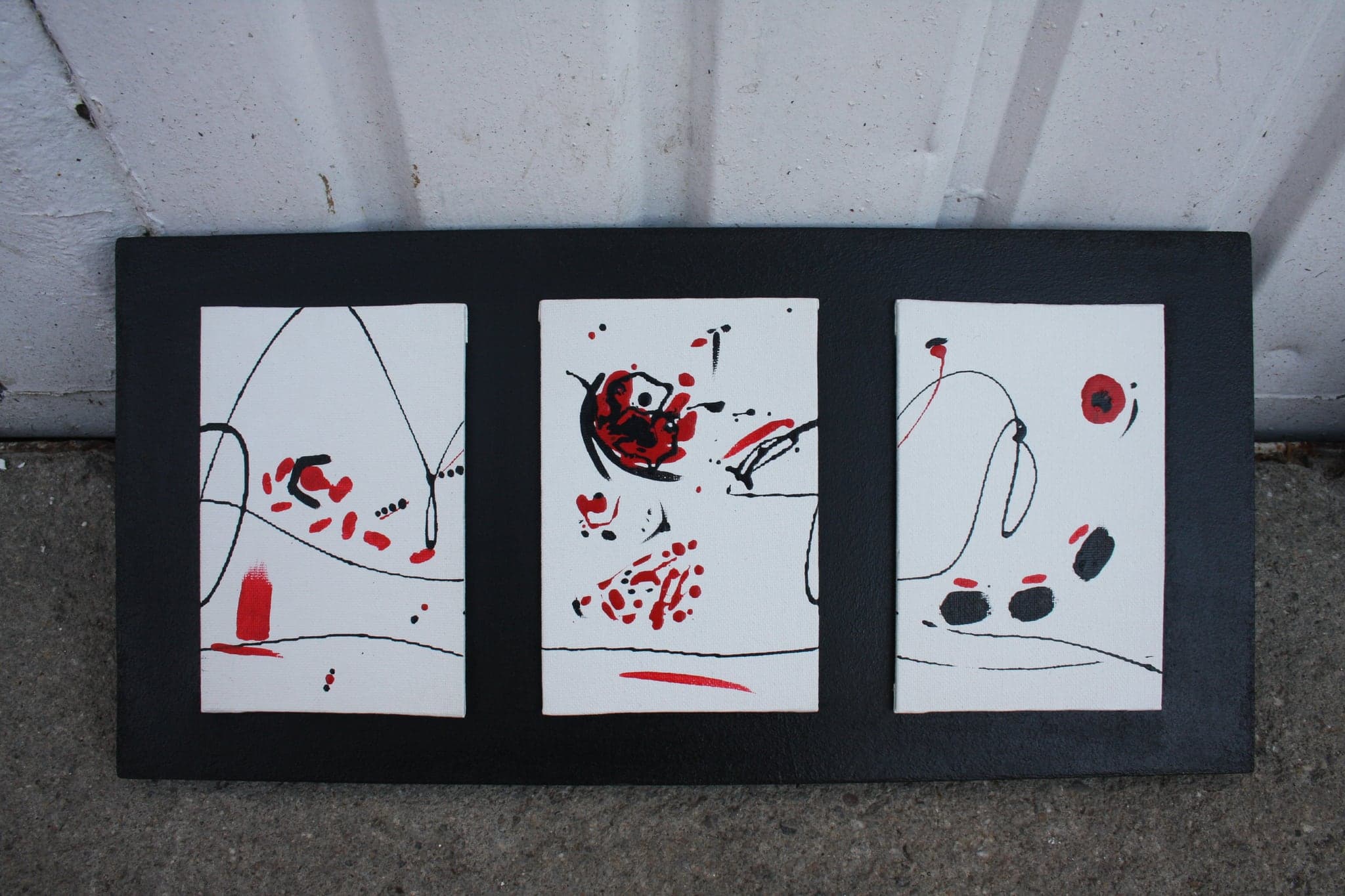 Three small works framed together in a single long black frame, leaning against a wall