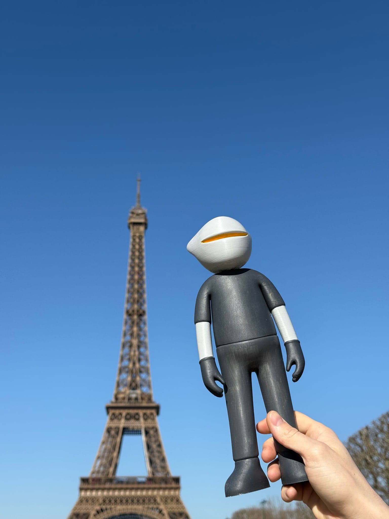 Mr. B held up in a hand against a clear blue sky, the Eiffel Tower standing behind him