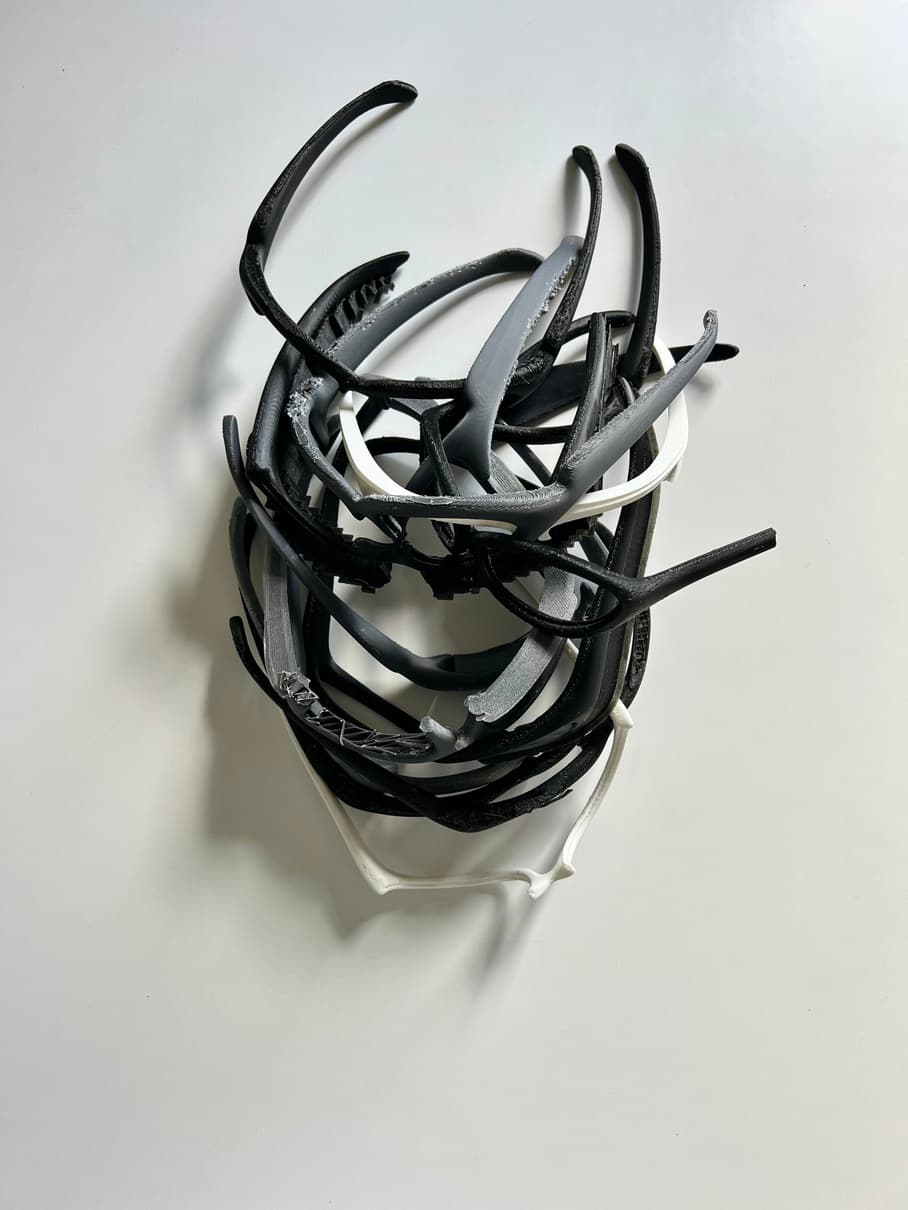 A pile of printed BRUT SHADES frames on a white table, a dozen or more, all black