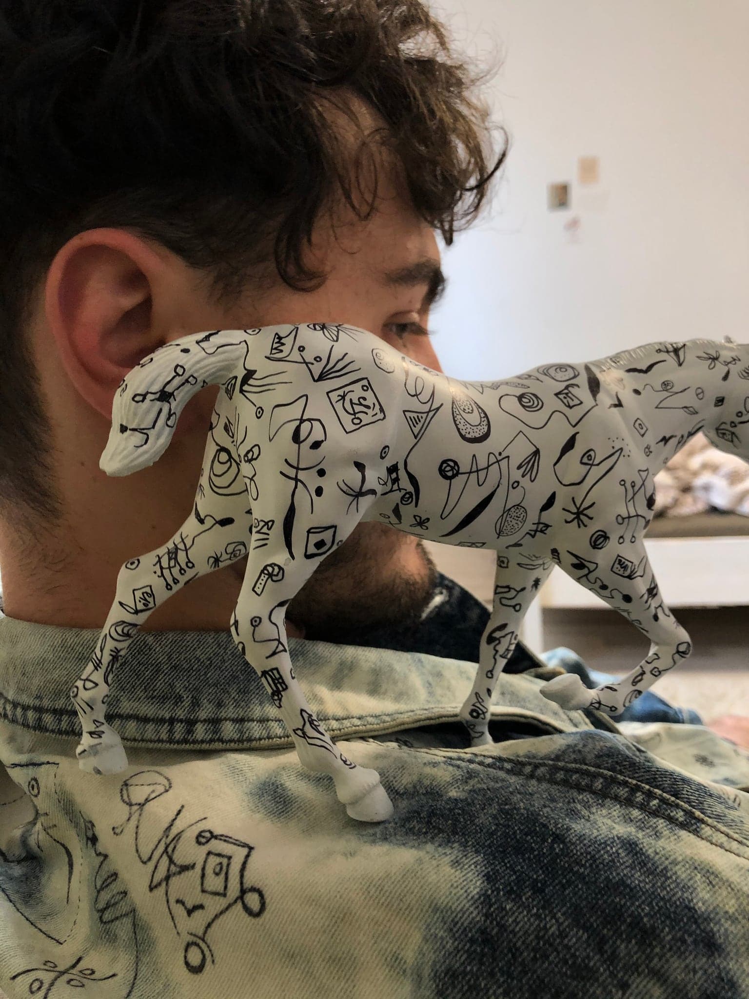 Close on the shoulder of the jacket with the small drawn paper horse standing on it, both carrying the same marks