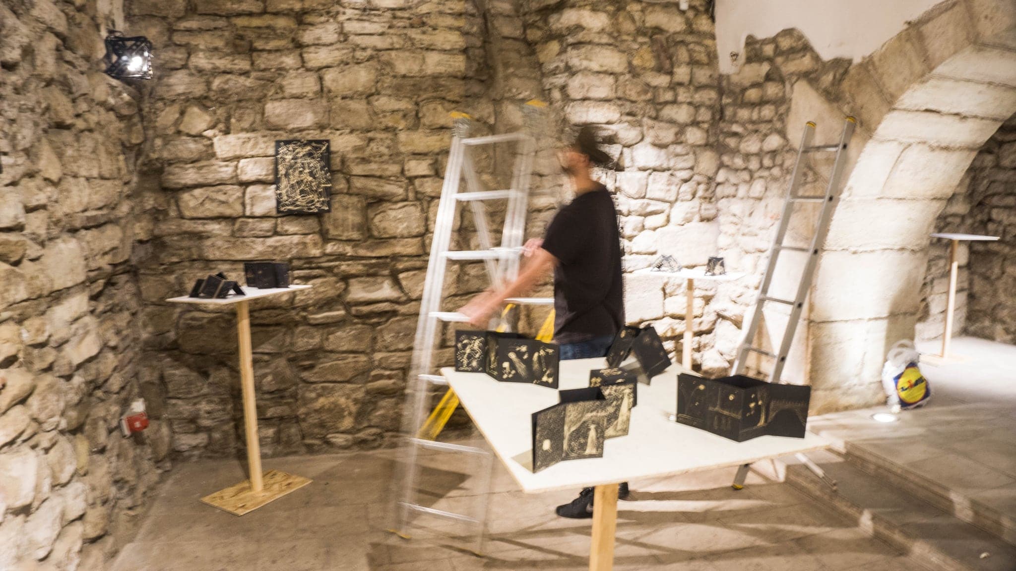 The same room during the install, a ladder against the stone wall and works being set out on a white table