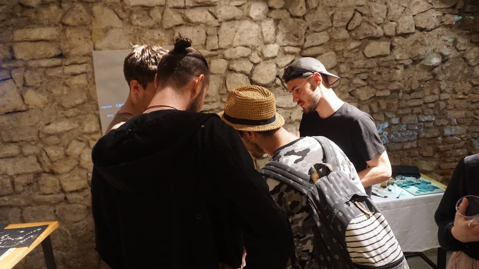 Several people leaning in close over a lit panel of drawings, absorbed, their backs to the camera