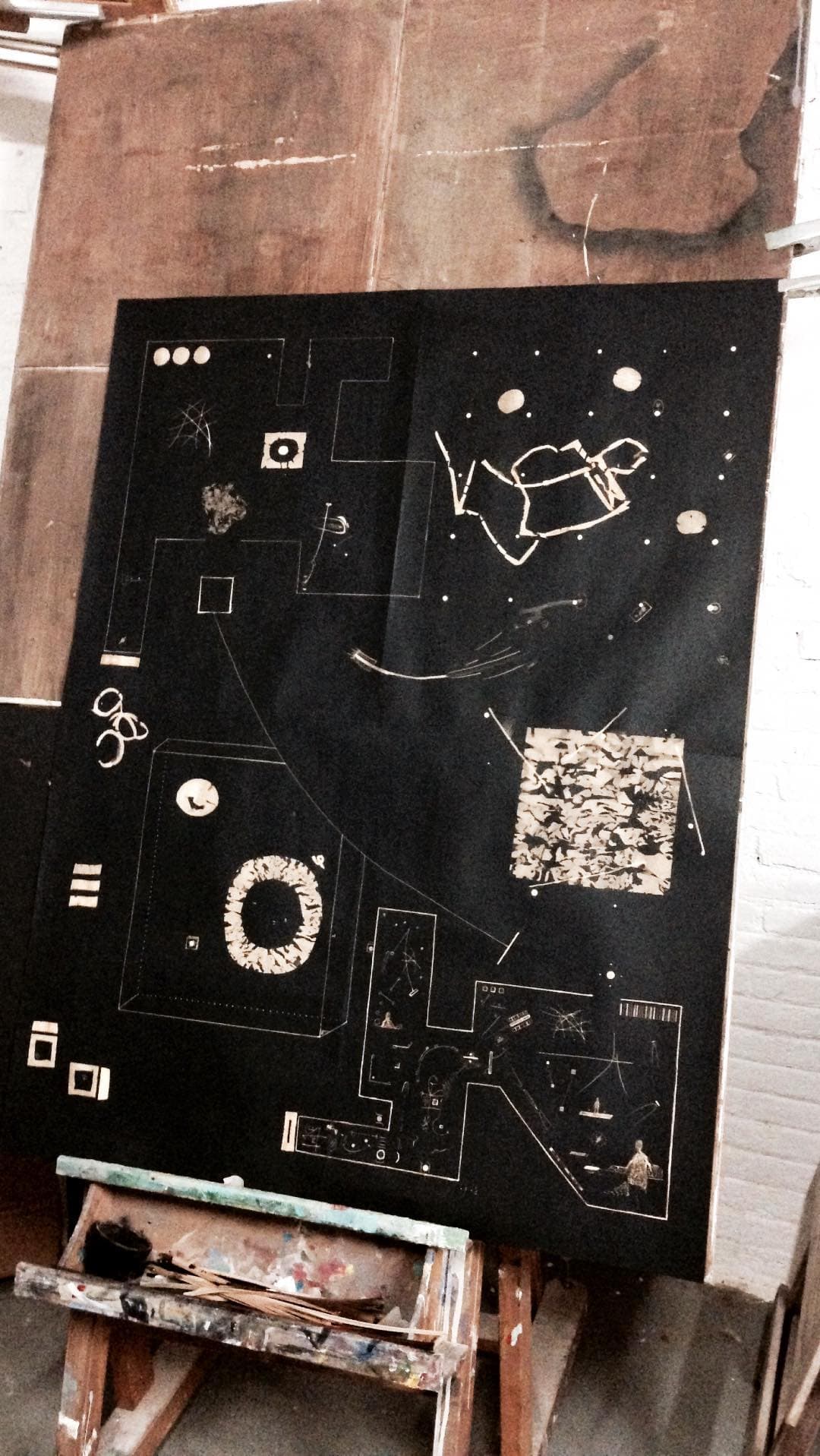 A large black board leaning in the studio, covered in symbols, a spiral and small framed marks