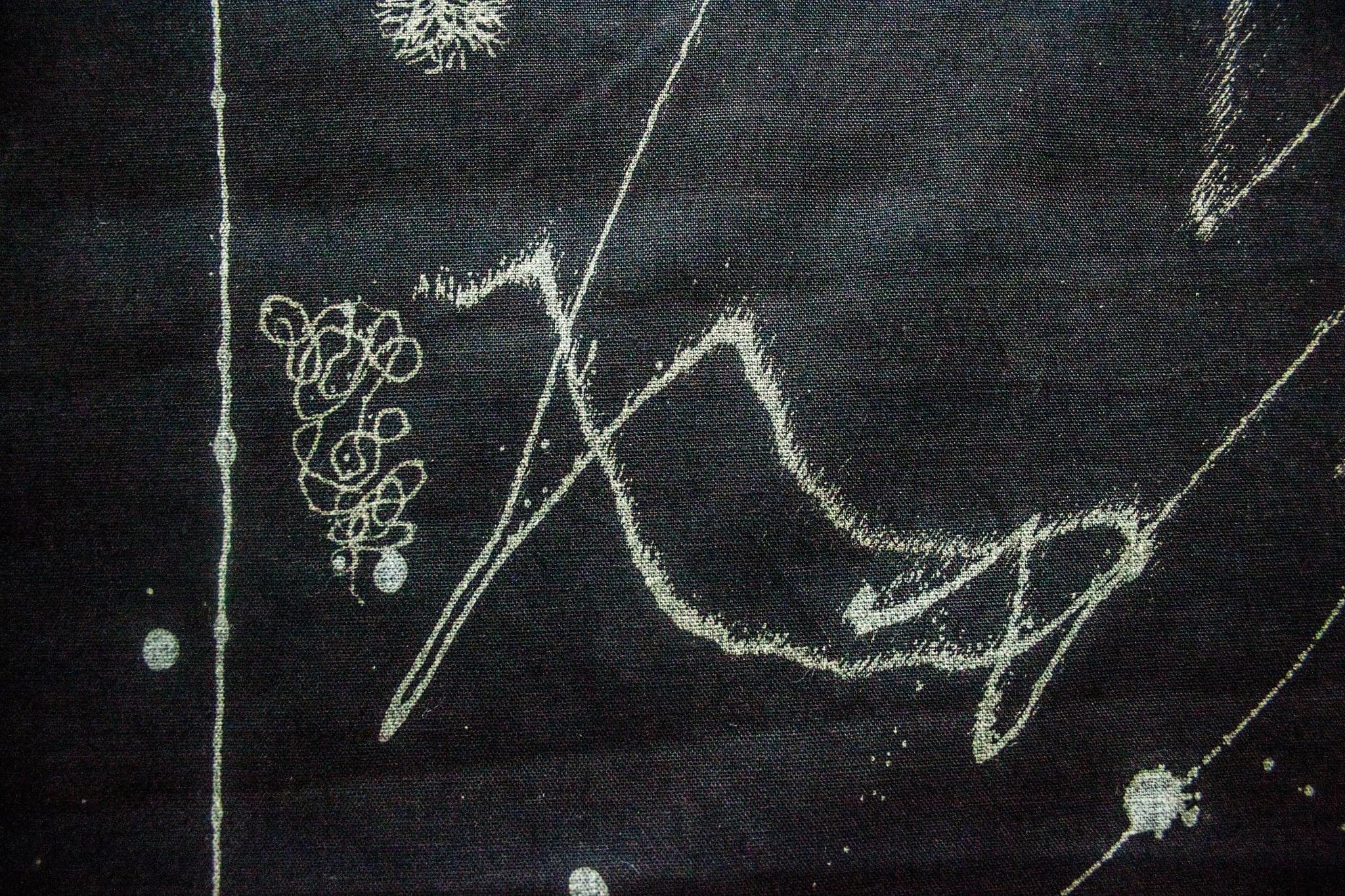 A second black cloth: loose pale loops and a long zig-zag stroke across the field, a tight knot of small circles at the left, a straight vertical run of bleach down the left side, and scattered round drips.