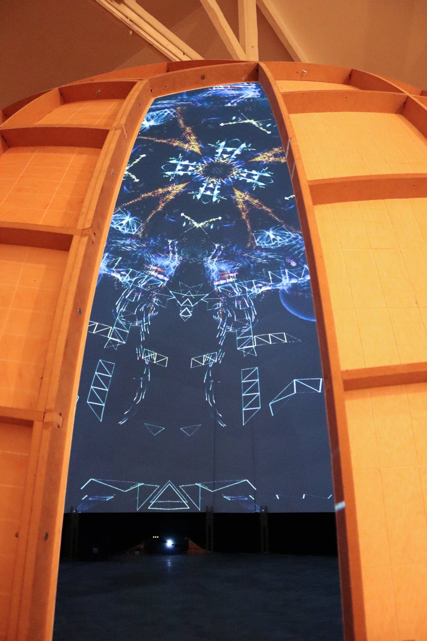 The dome's tall arched doorway seen close, warm plywood ribs framing a dark blue interior scattered with drawn white line