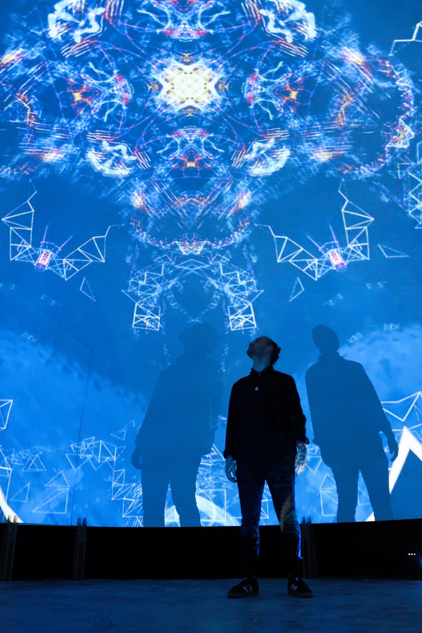 Three figures in silhouette standing under a blue eight-fold mandala that covers the whole curved wall