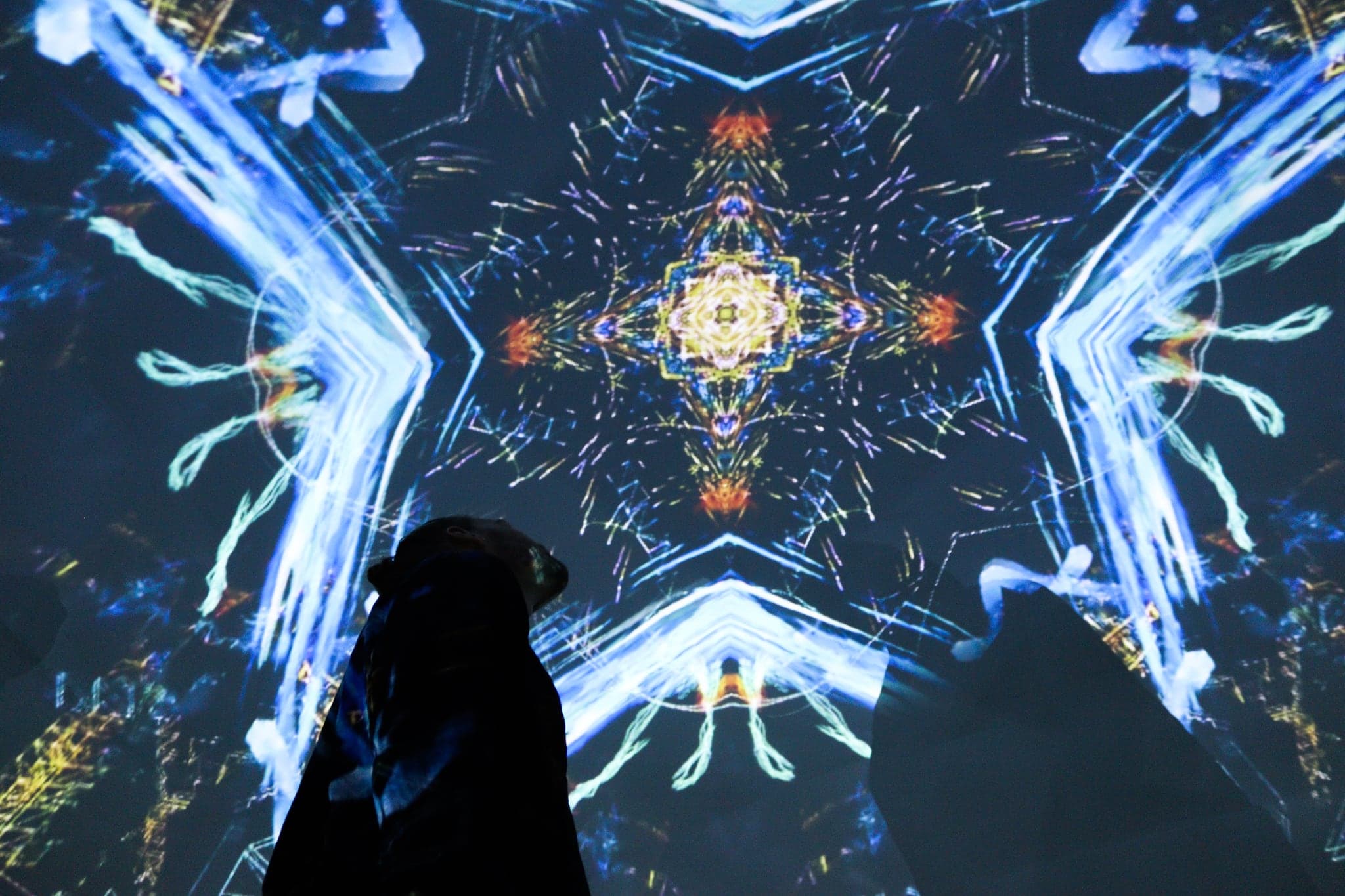 A symmetrical burst of white and gold line radiating from a small jewelled centre, a figure crouched dark at the lower edge