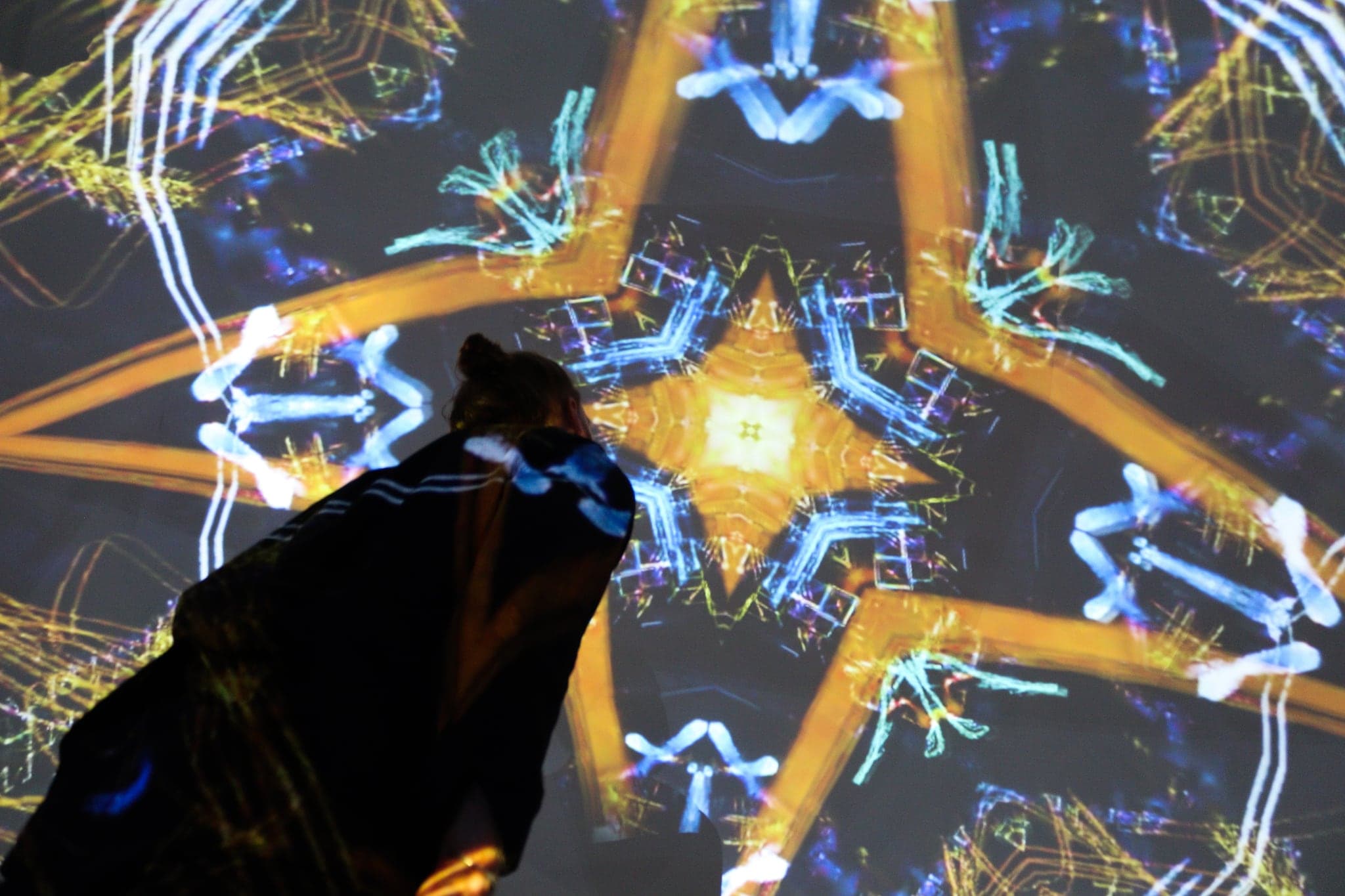 A large gold star of thick painted line over cyan scribble, a person's shoulder and head passing dark through the beam