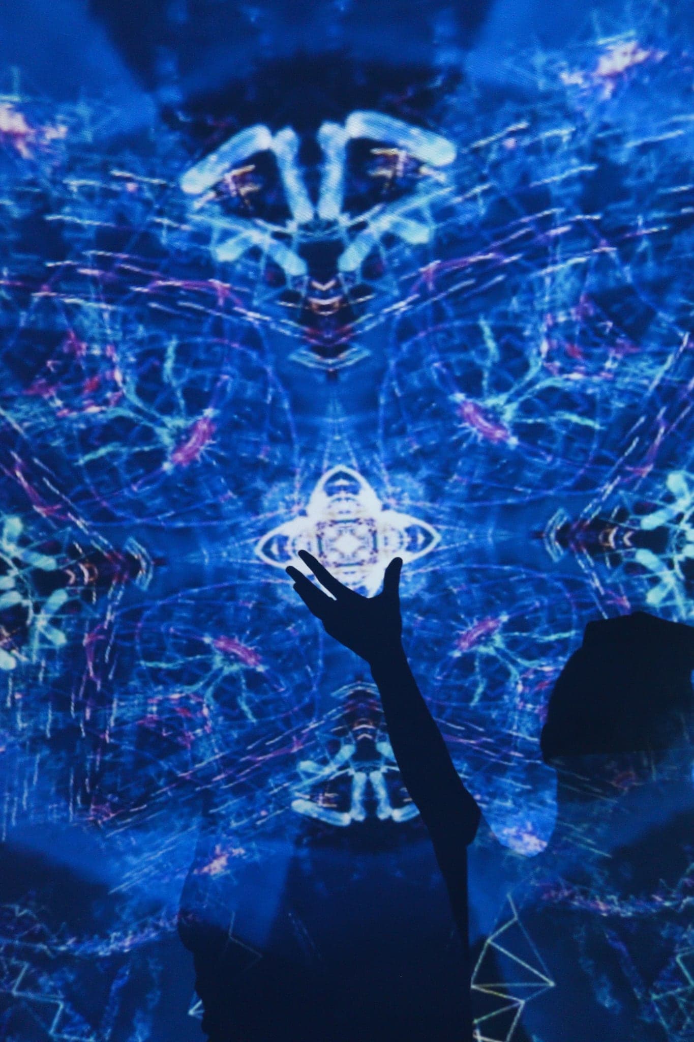 A silhouetted figure reaching one arm up into a dense blue field of mirrored drawing