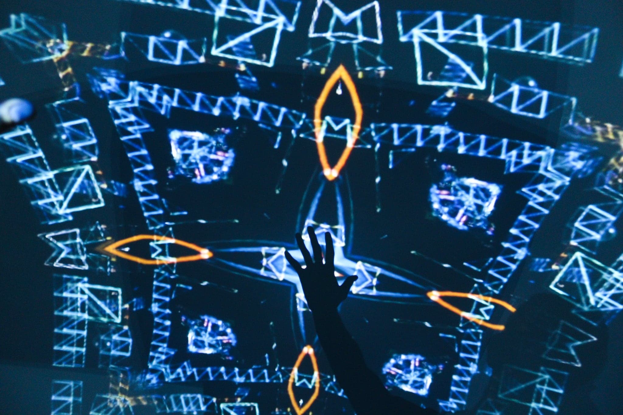 An open hand held up against a projected cyan grid of wire triangles and small orange lozenges