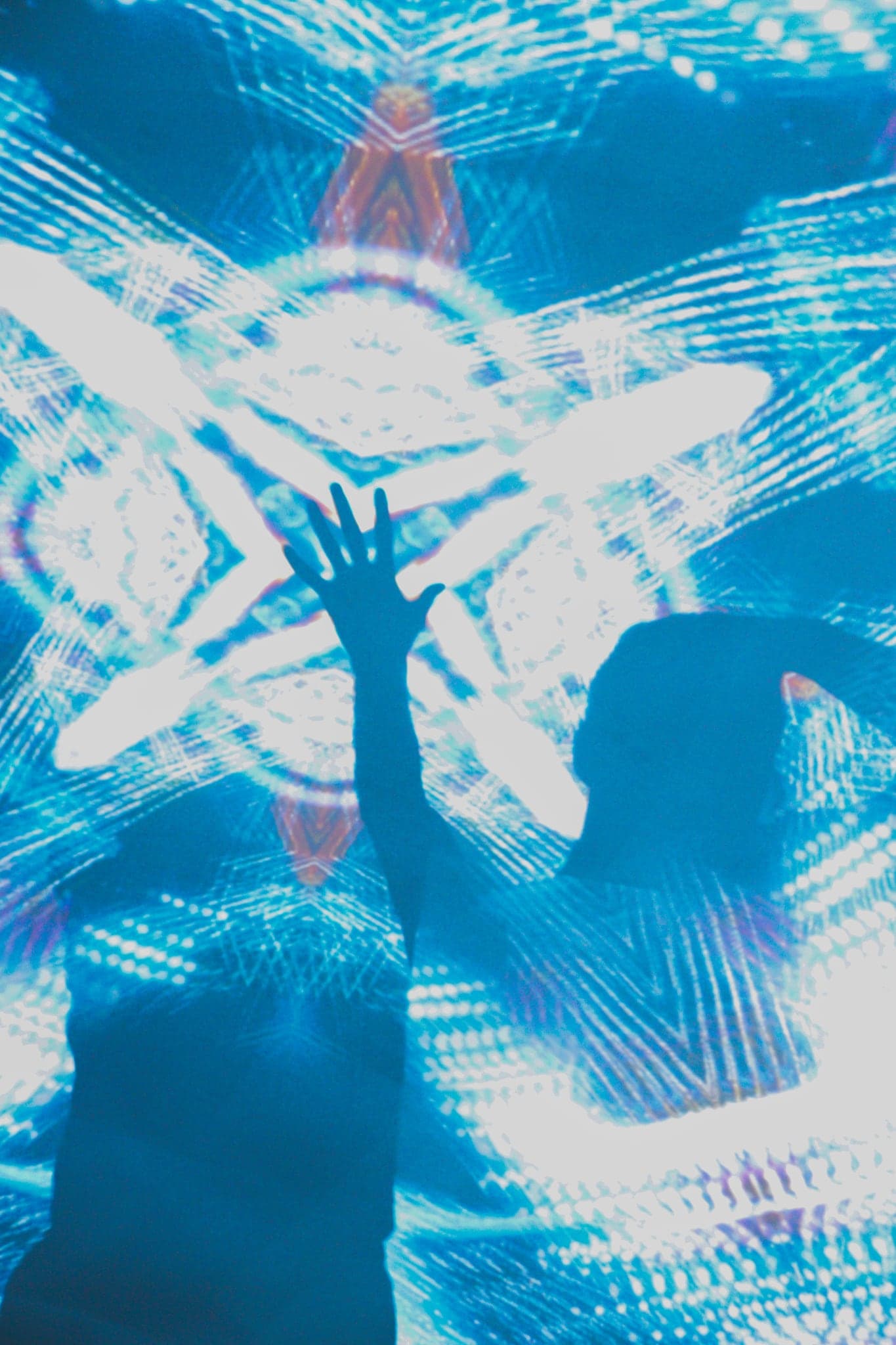 Two hands raised together inside a large white projected shape, their shadow spreading like wings across the dome
