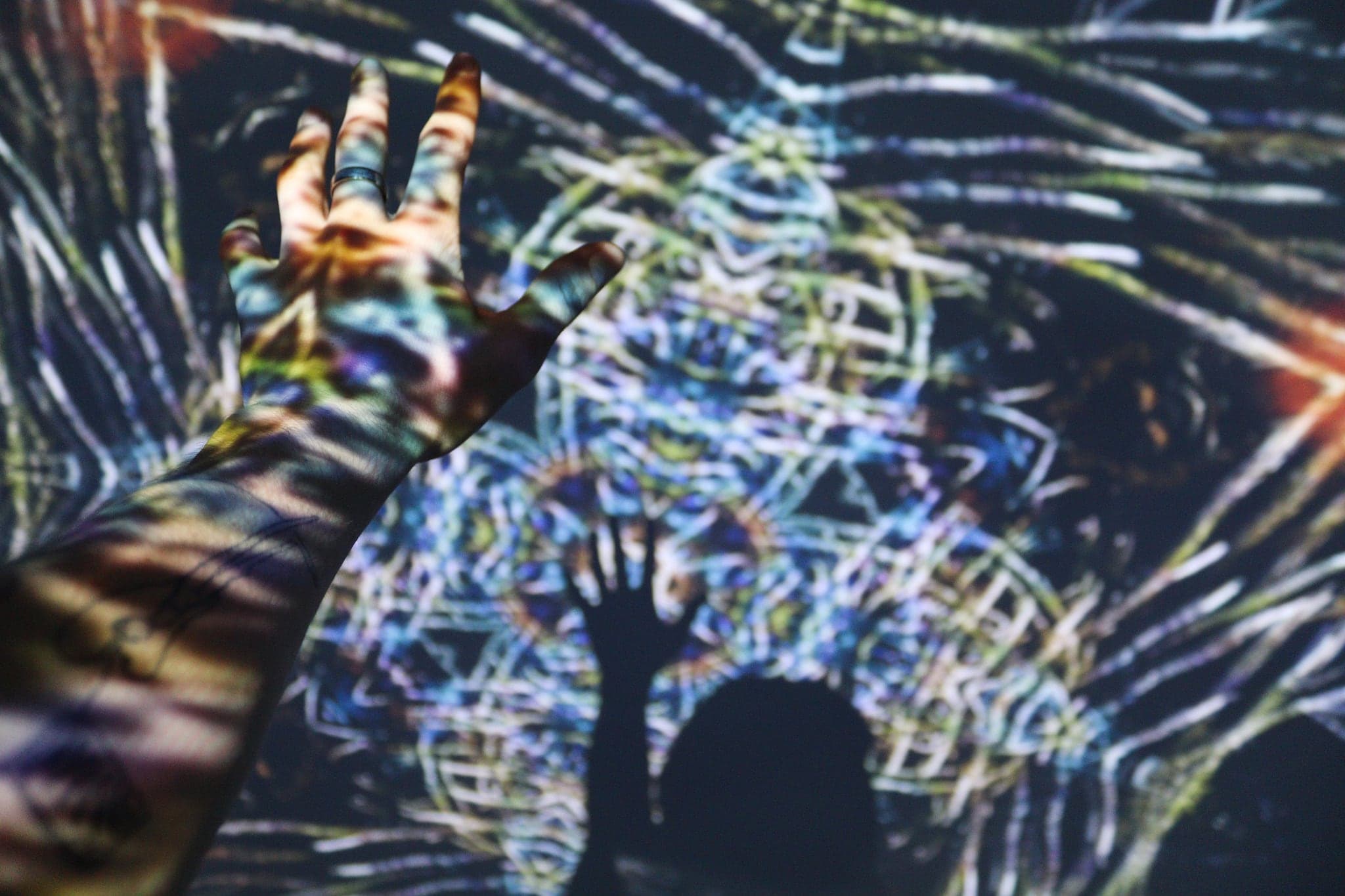 A hand open in the projector beam, the drawn line painting itself across the skin in yellow and white