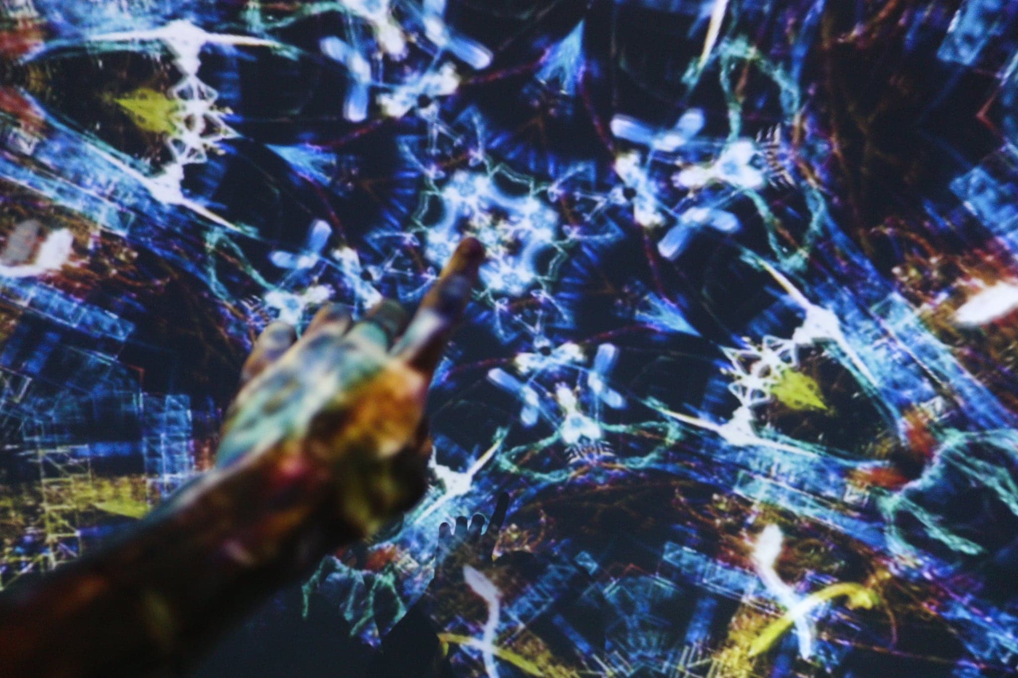 An arm lifted into a loose yellow scribble of light, blue filaments trailing behind it across the curved wall