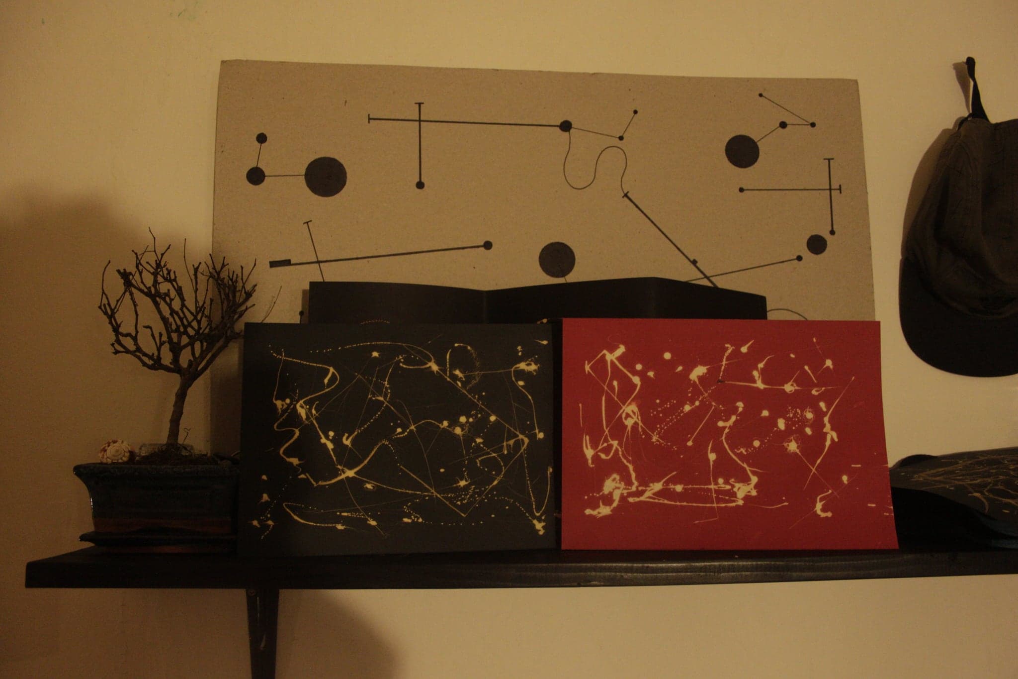 A black board marked with dots and connecting lines mounted on a wall, with a gold-marked black sheet and a red sheet standing on the shelf below