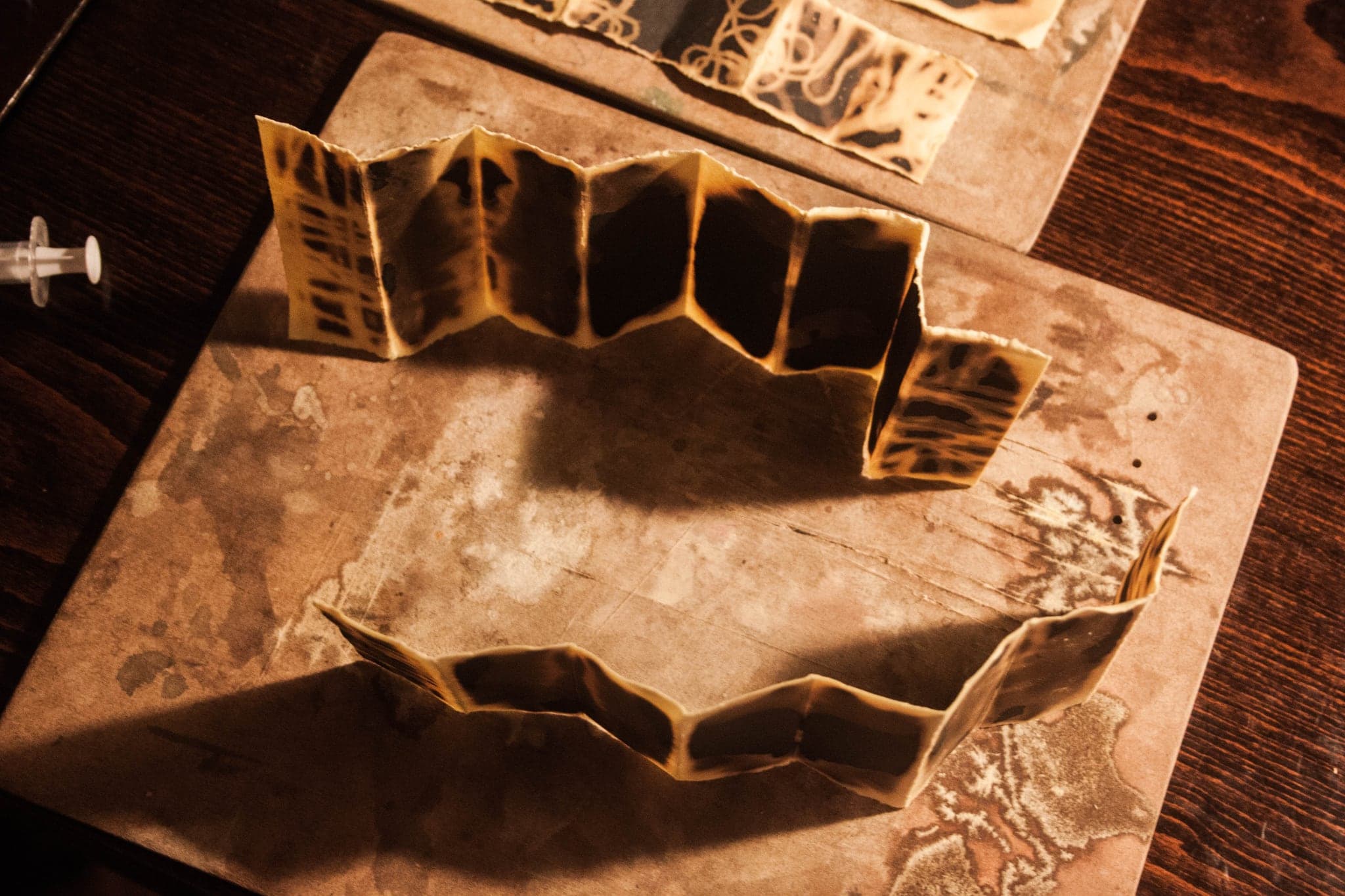 One book standing open on a dark table, its folds catching the light so the creases glow amber against the black paper.