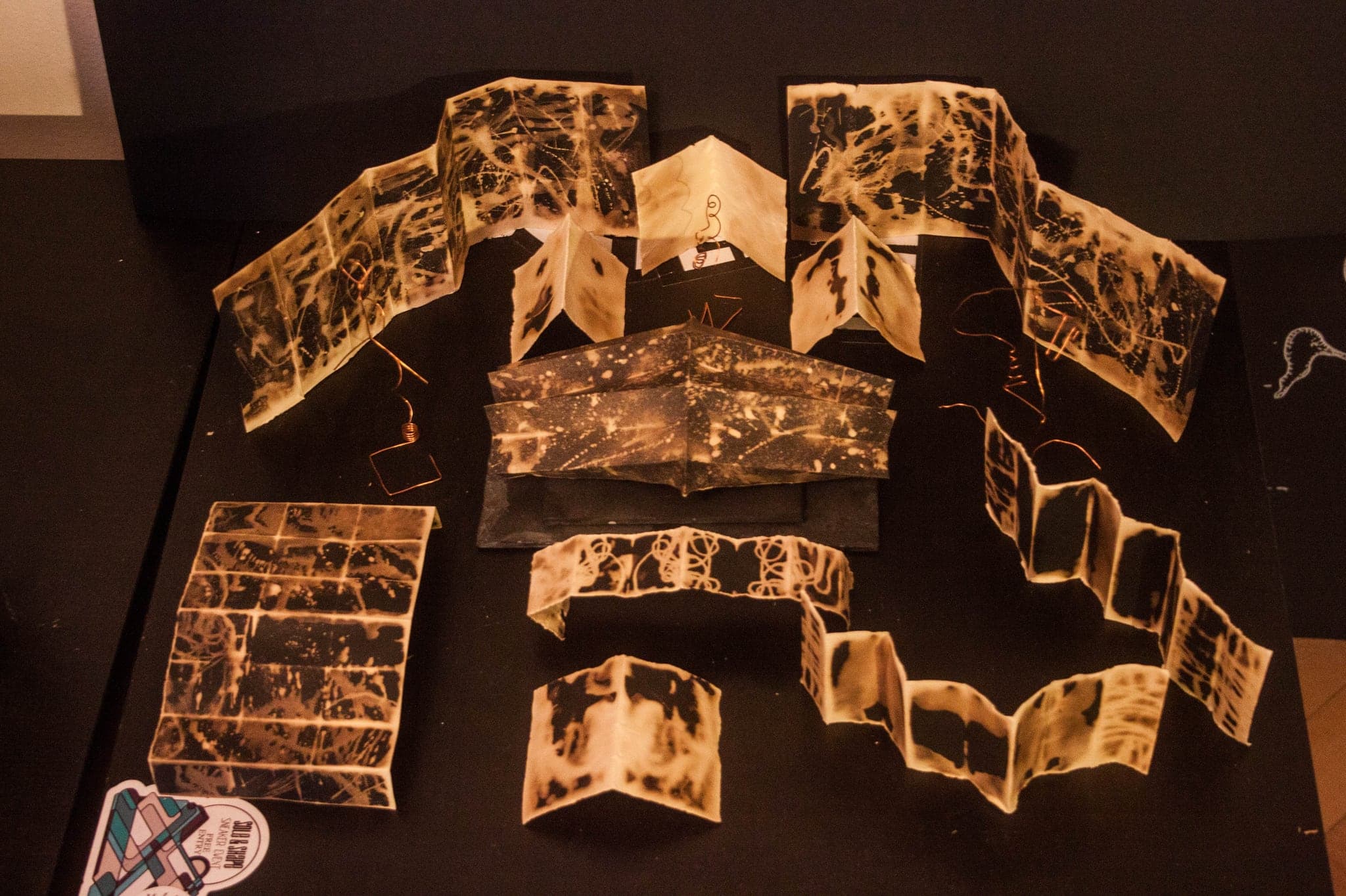 Many of the books opened out across a dark surface, seen from above, their pages spread into a loose field of pale marks.