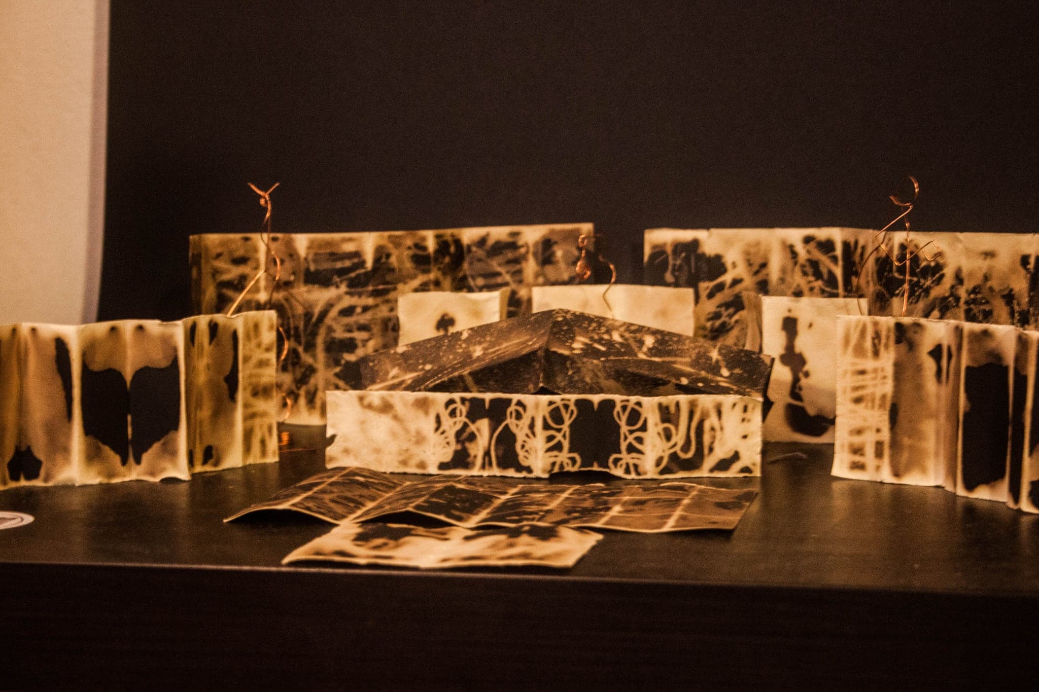 Several books open on a table in a dim room, warm light raking across them and loose sheets lying in front.