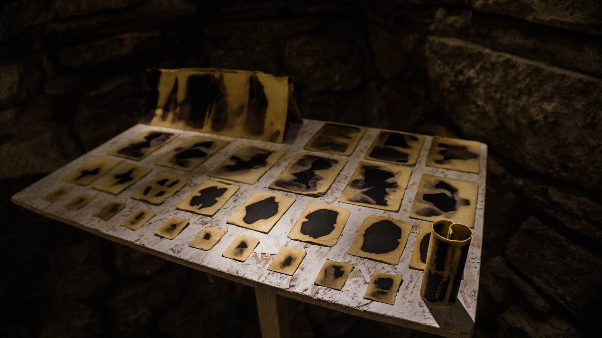 A long table in a stone-vaulted room carrying a grid of small bleached cards, lit warm against the bare walls.
