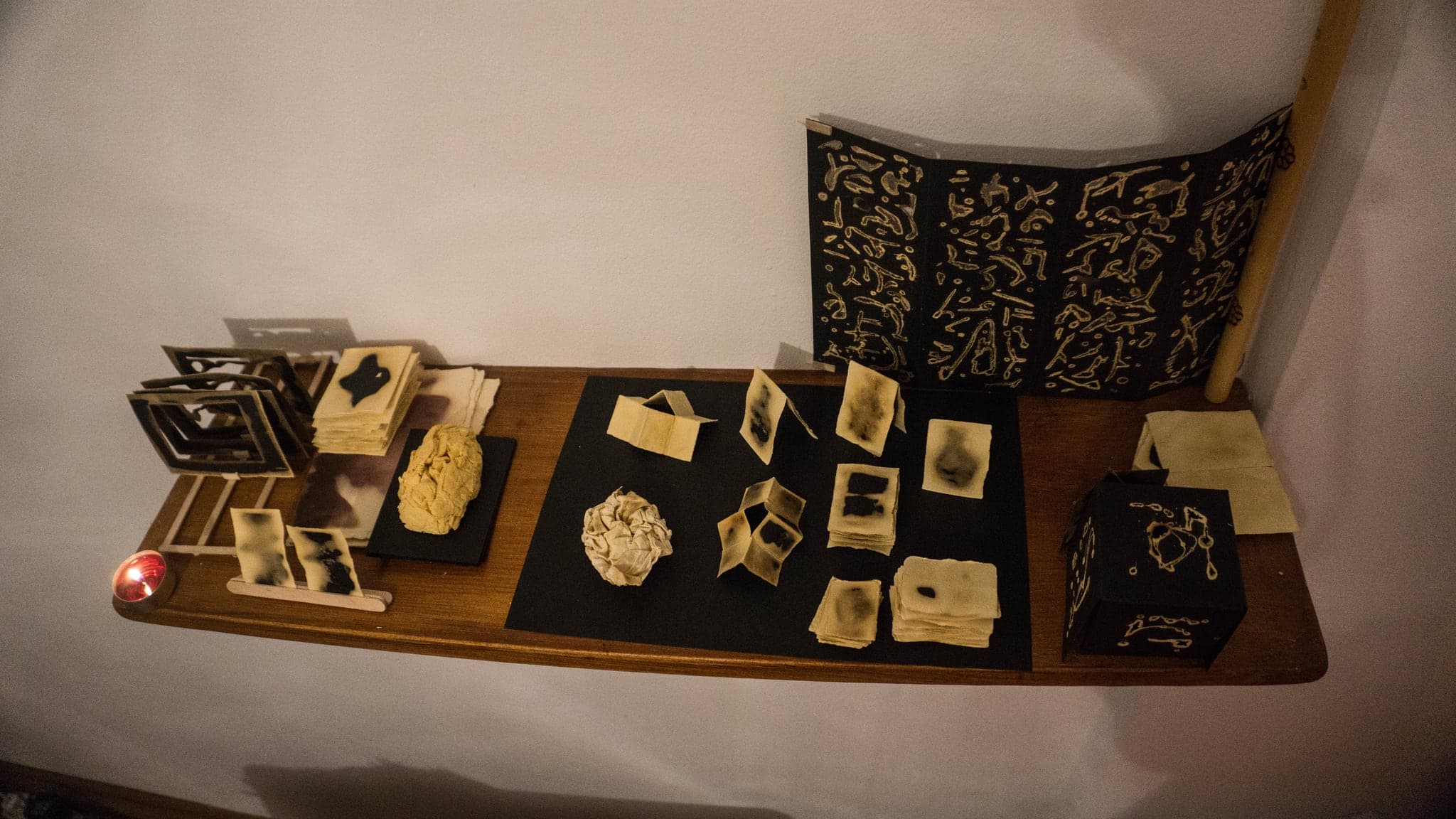 A display table against a white wall: small cards set out in rows, a black panel of marks standing behind them.