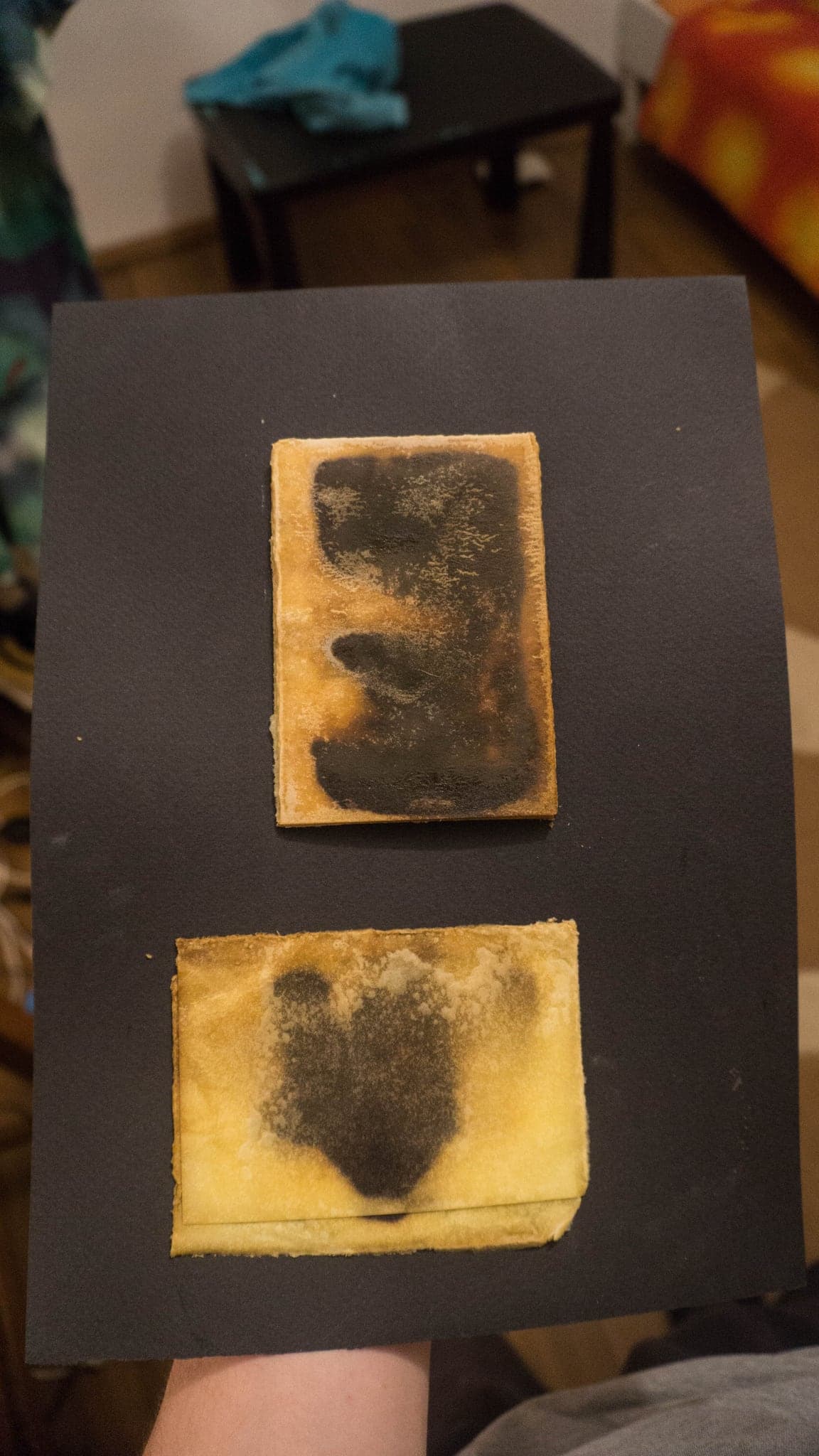 A hand holding a black board with two small cards mounted on it, one dark and one yellowed.