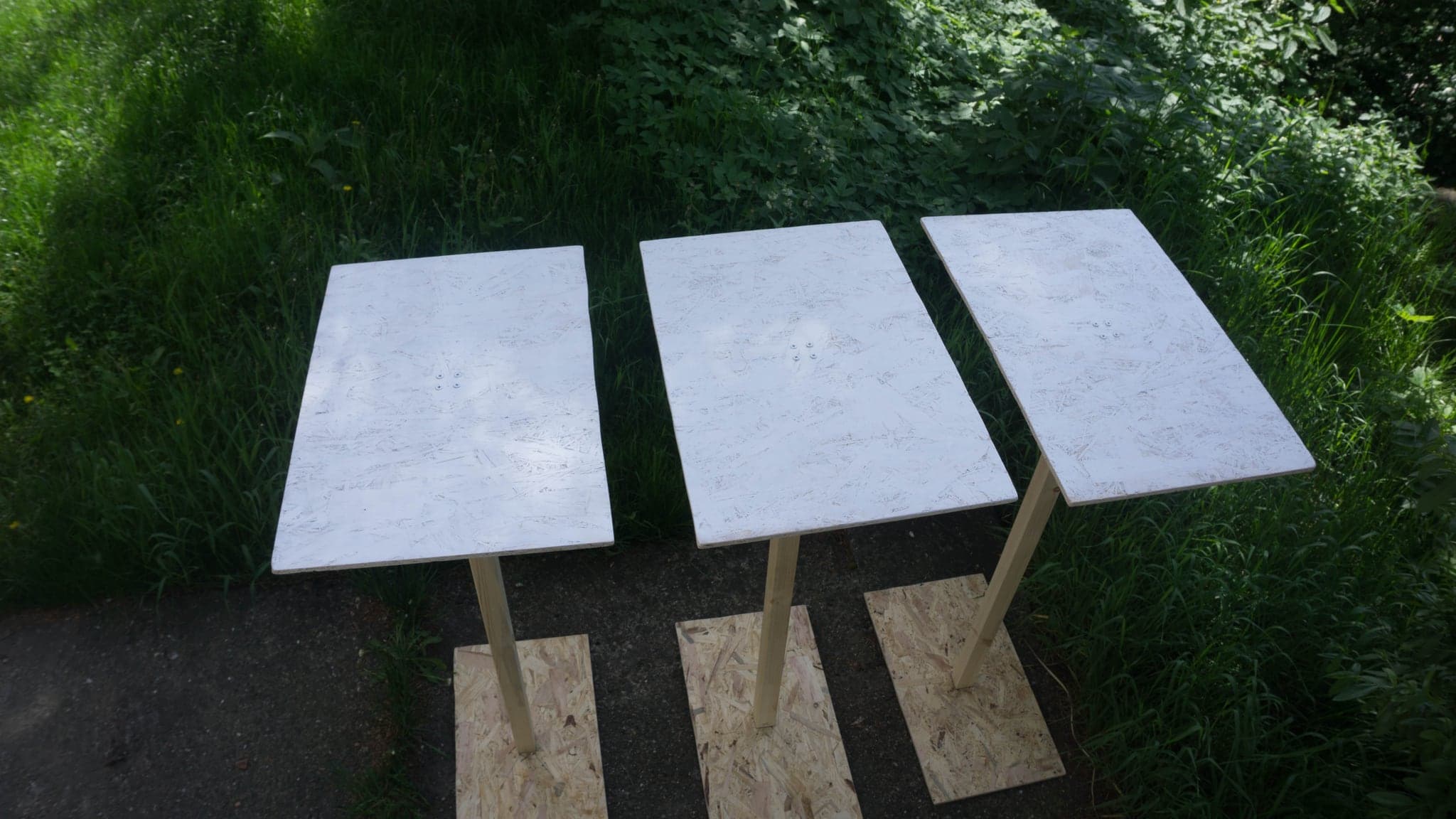 Three white panels on wooden legs standing outdoors on grass in daylight.