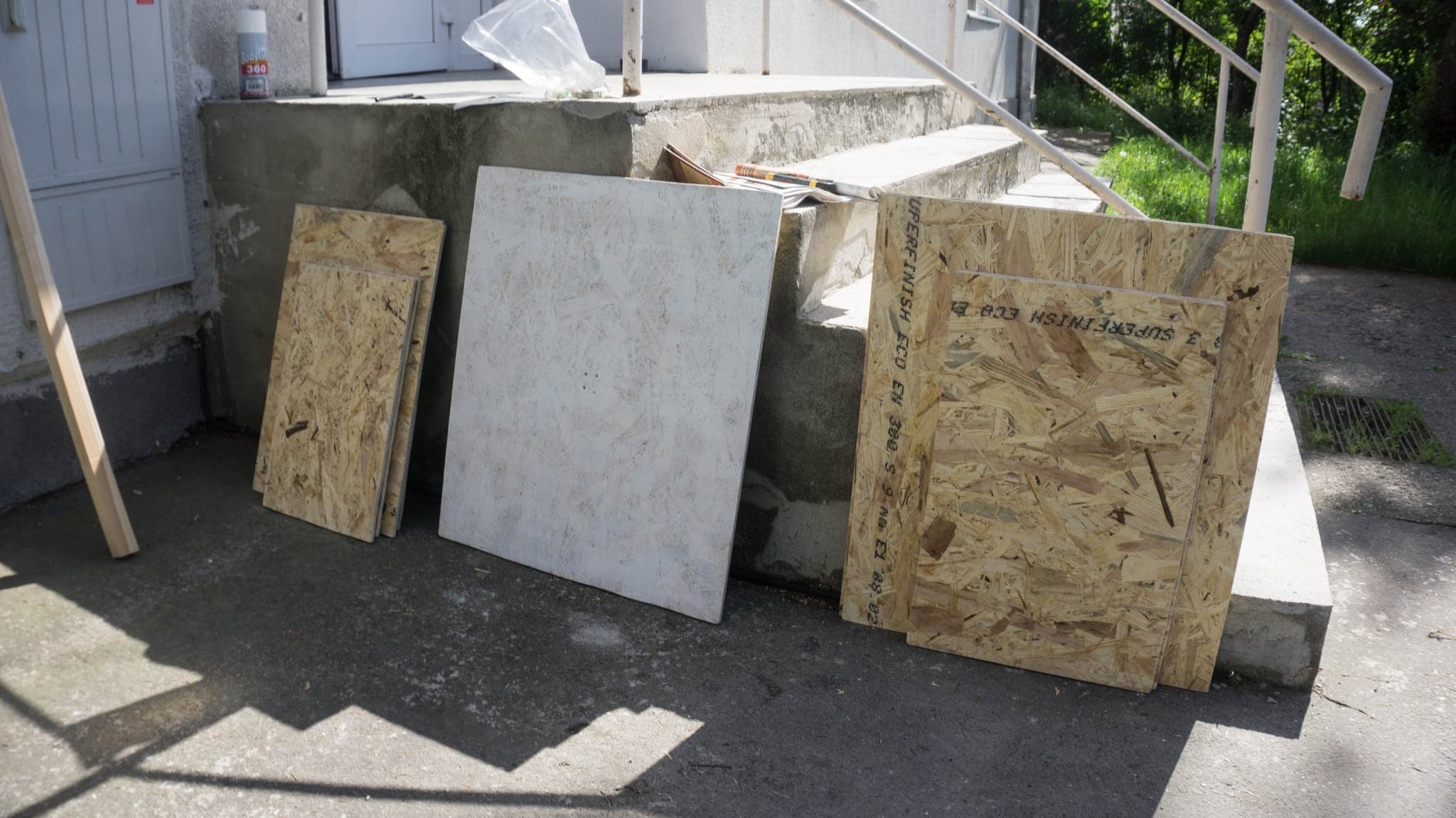 Three boards leaning against a concrete step in bright sun, their surfaces pale and worked.