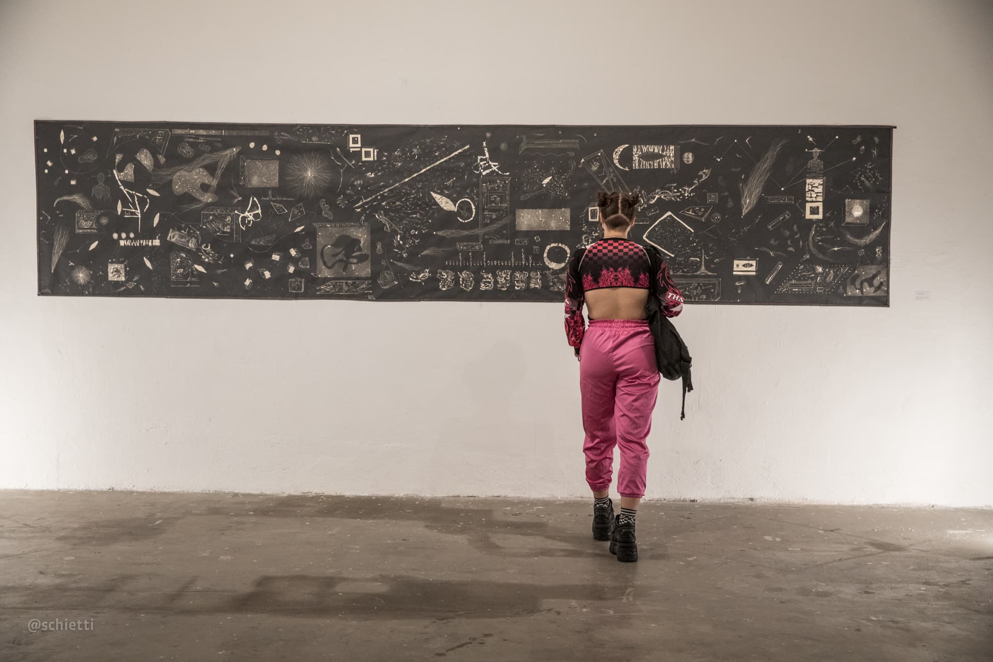 The five metre panel across a white gallery wall, one visitor walking past it for scale