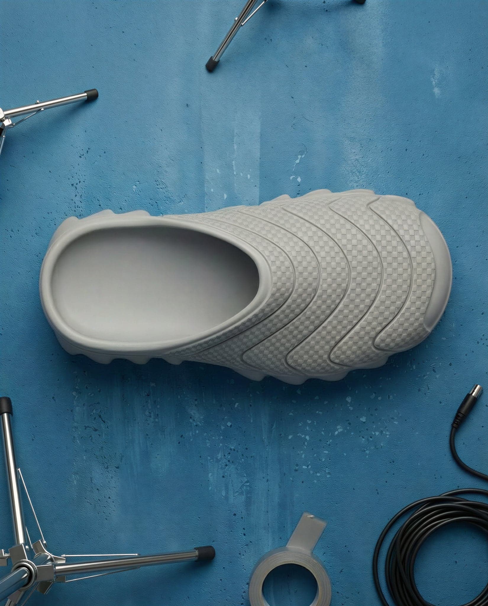 A single grey mule seen from above at an angle on a blue floor, showing the open heel and deep oval collar.