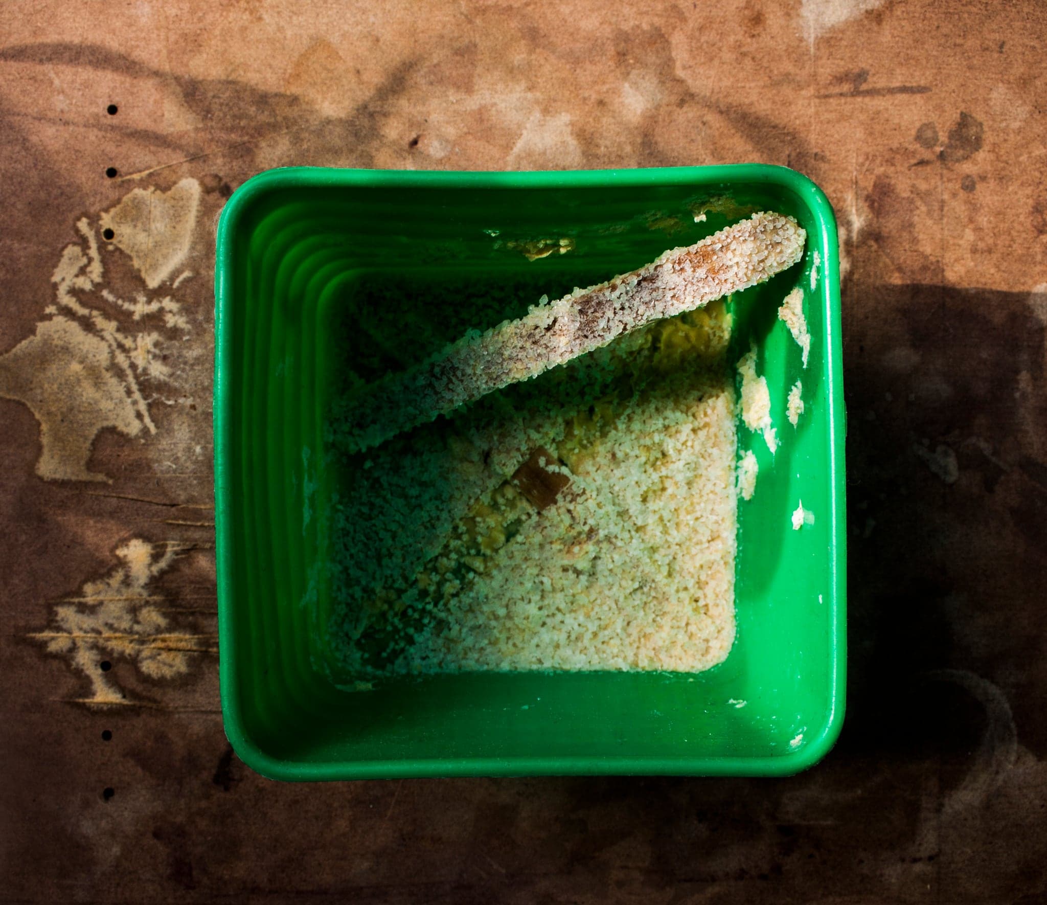 A green plastic tray on the bench holding a white crust, one treated piece resting in it.