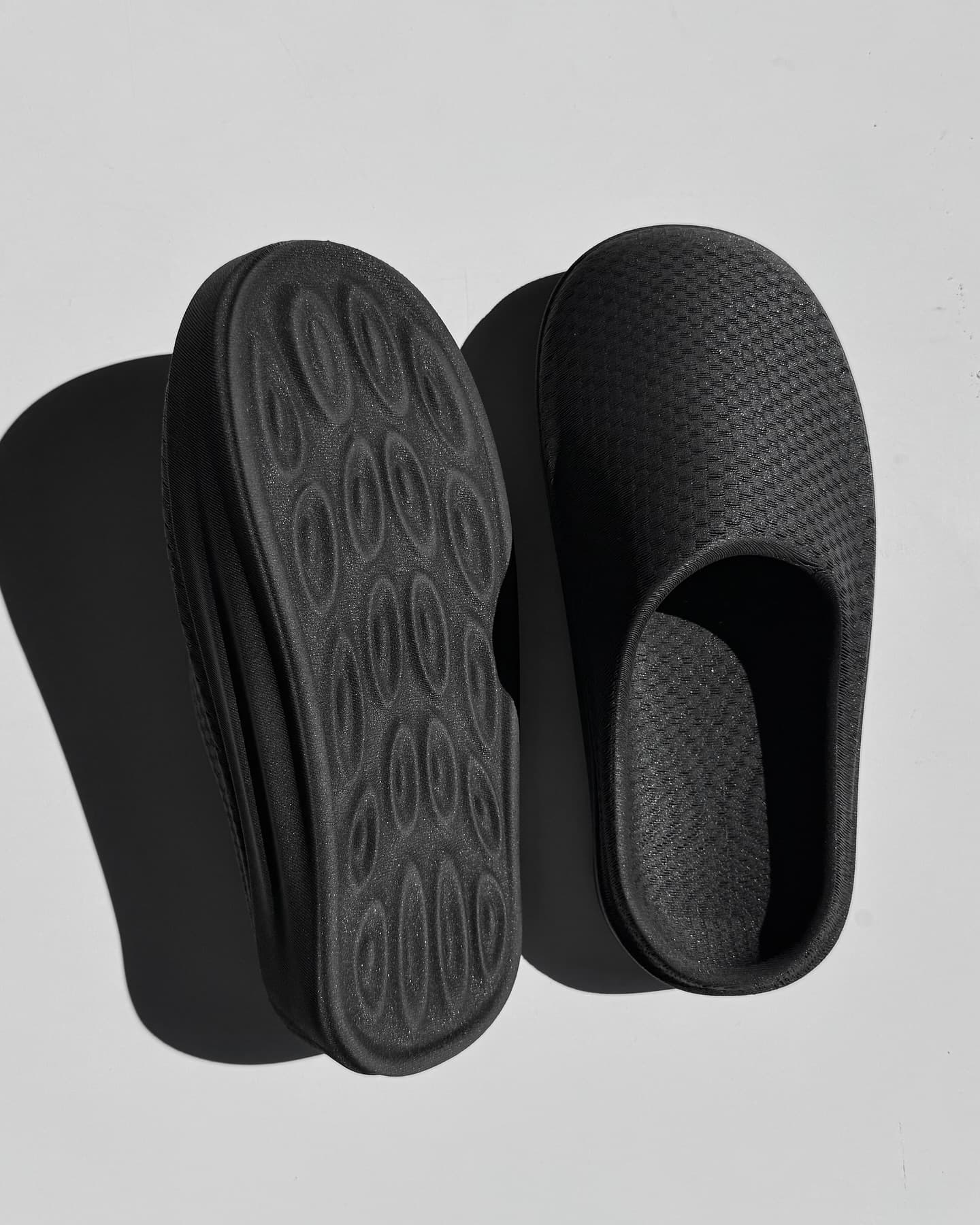 The physical NEVO pair in sunlight, one shoe flipped to show the oval-lug sole