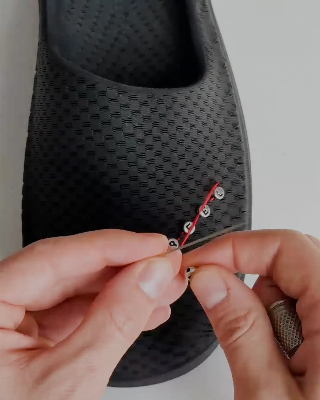 A hand wearing a thimble pushing the needle through the printed upper to fix a bead in place