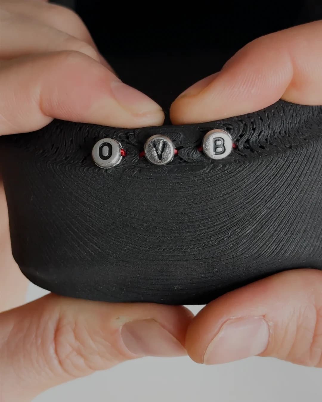 Macro of three lettered beads spelling O, V, B sewn into the printed weave of the black upper