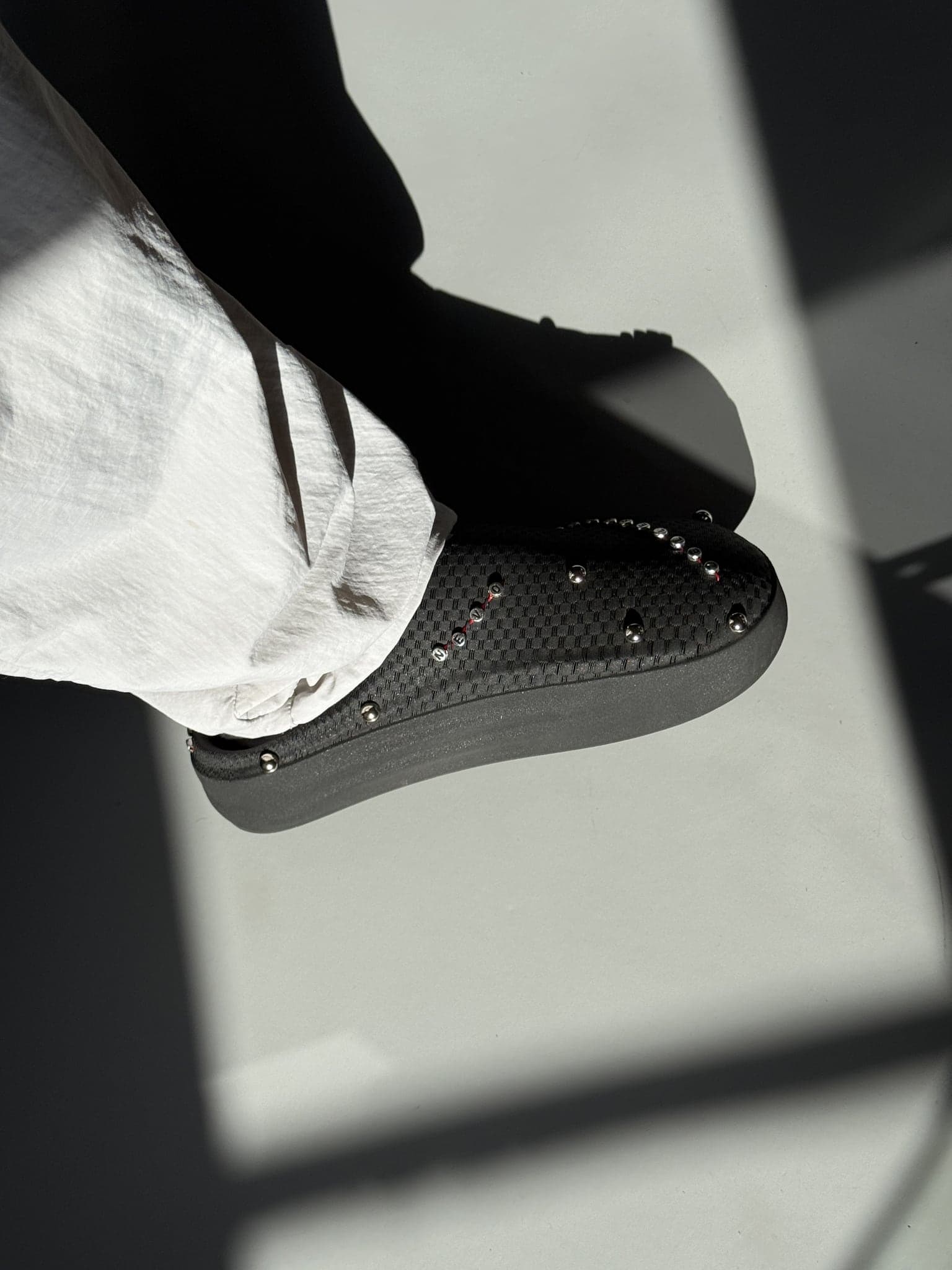The shoe worn in strong directional light, a hard shadow cutting across the foot and the studded flank