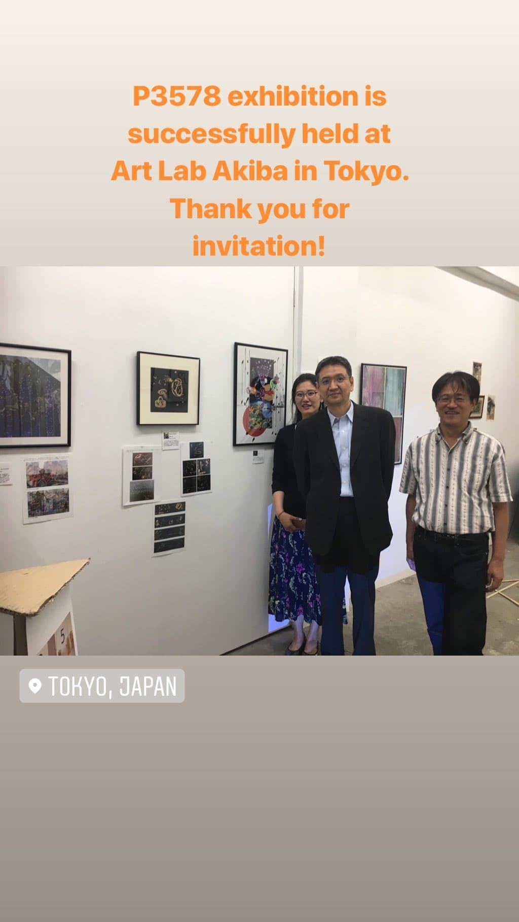 Three people standing in front of the exhibition wall at Art Lab Akiba, framed and unframed works hung around them