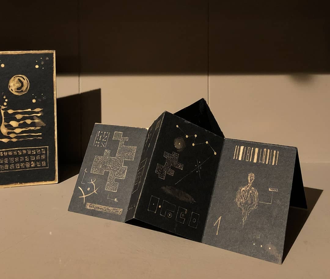 One copy standing open on a plinth, its folded pages holding it up like a screen