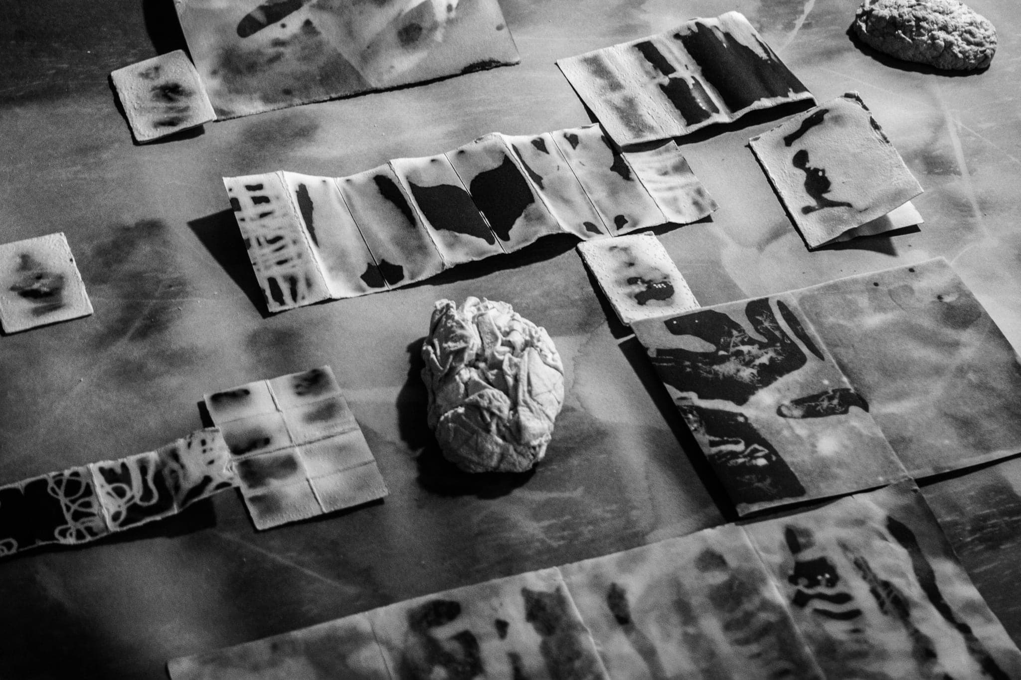 Low-angle black and white view along a table of pale wax tiles casting shadows, a crumpled ball of wax at the centre.