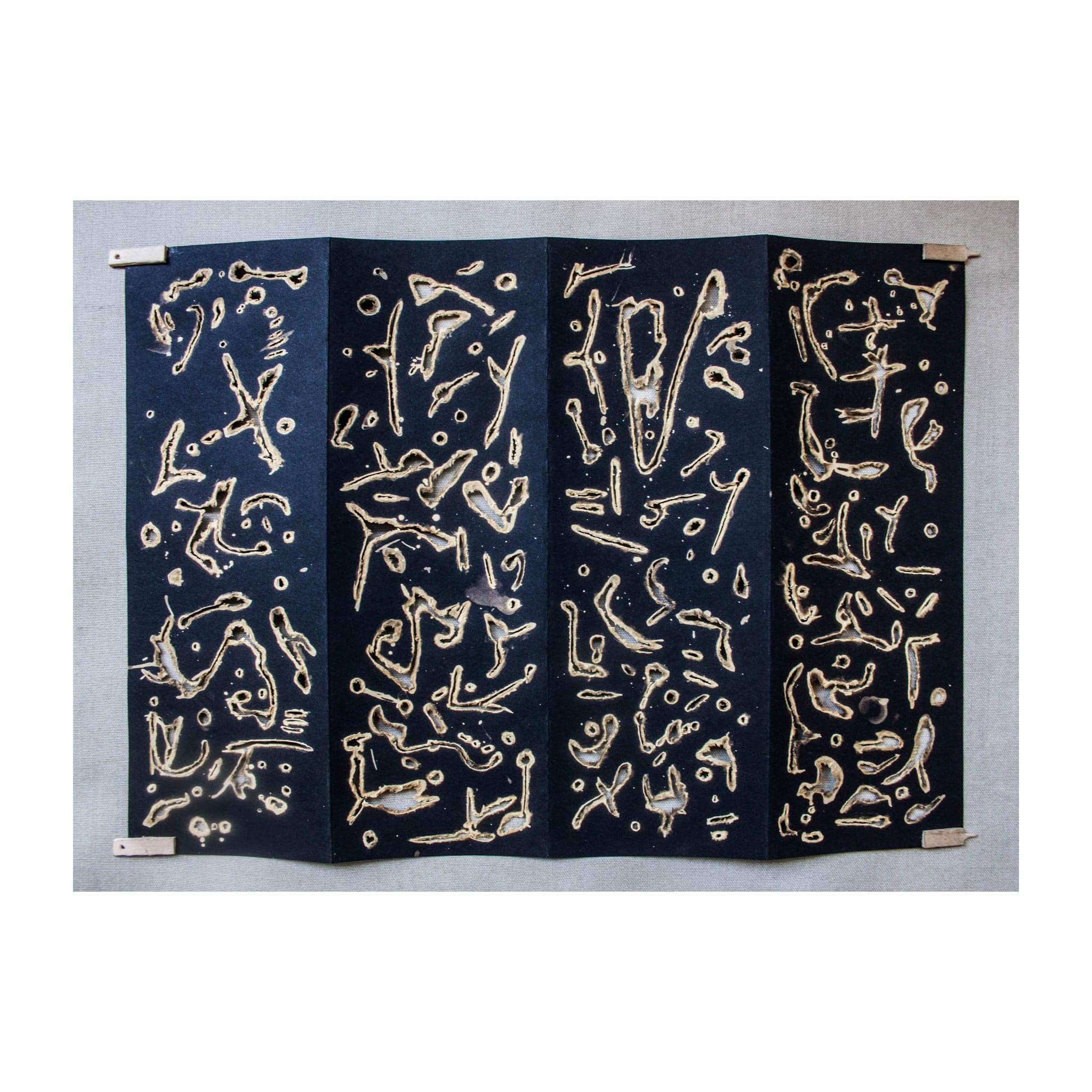 TOTEM opened out flat, four hinged panels pinned at the corners, marks running edge to edge