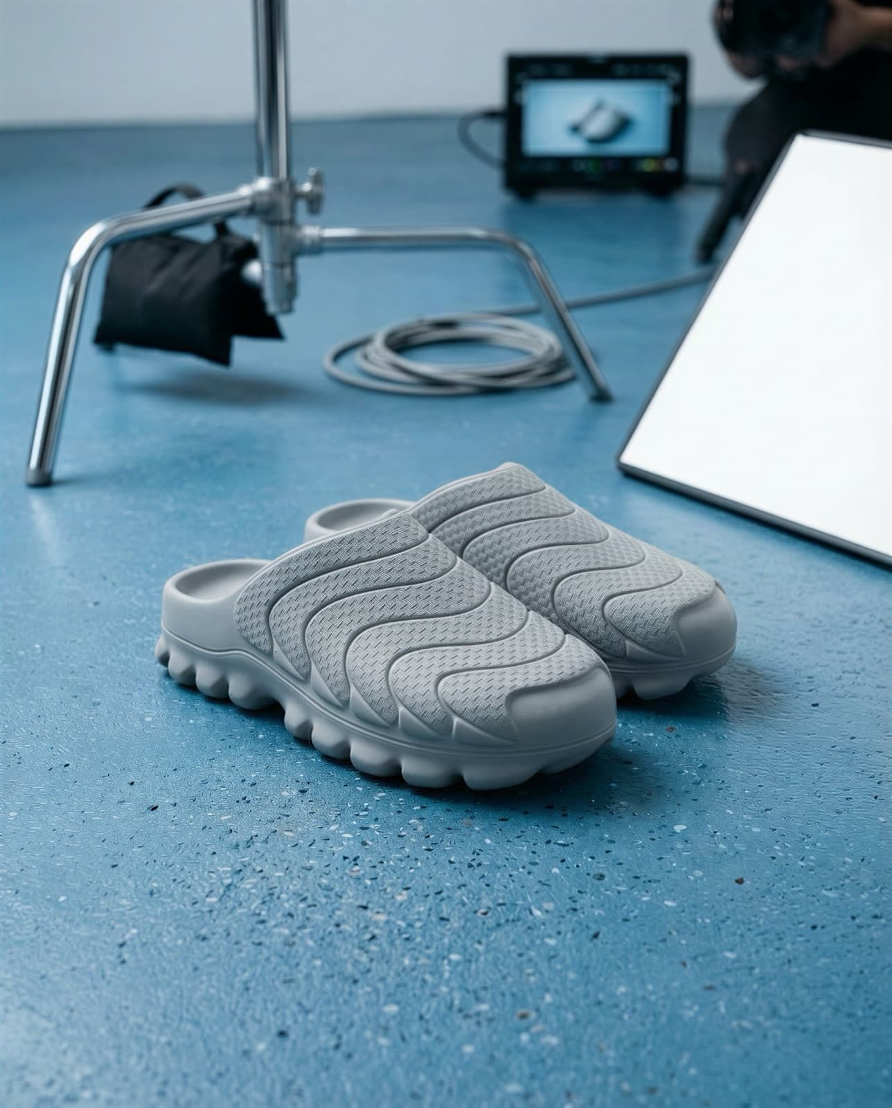 The KOVA mules on a blue studio set beside a lighting stand