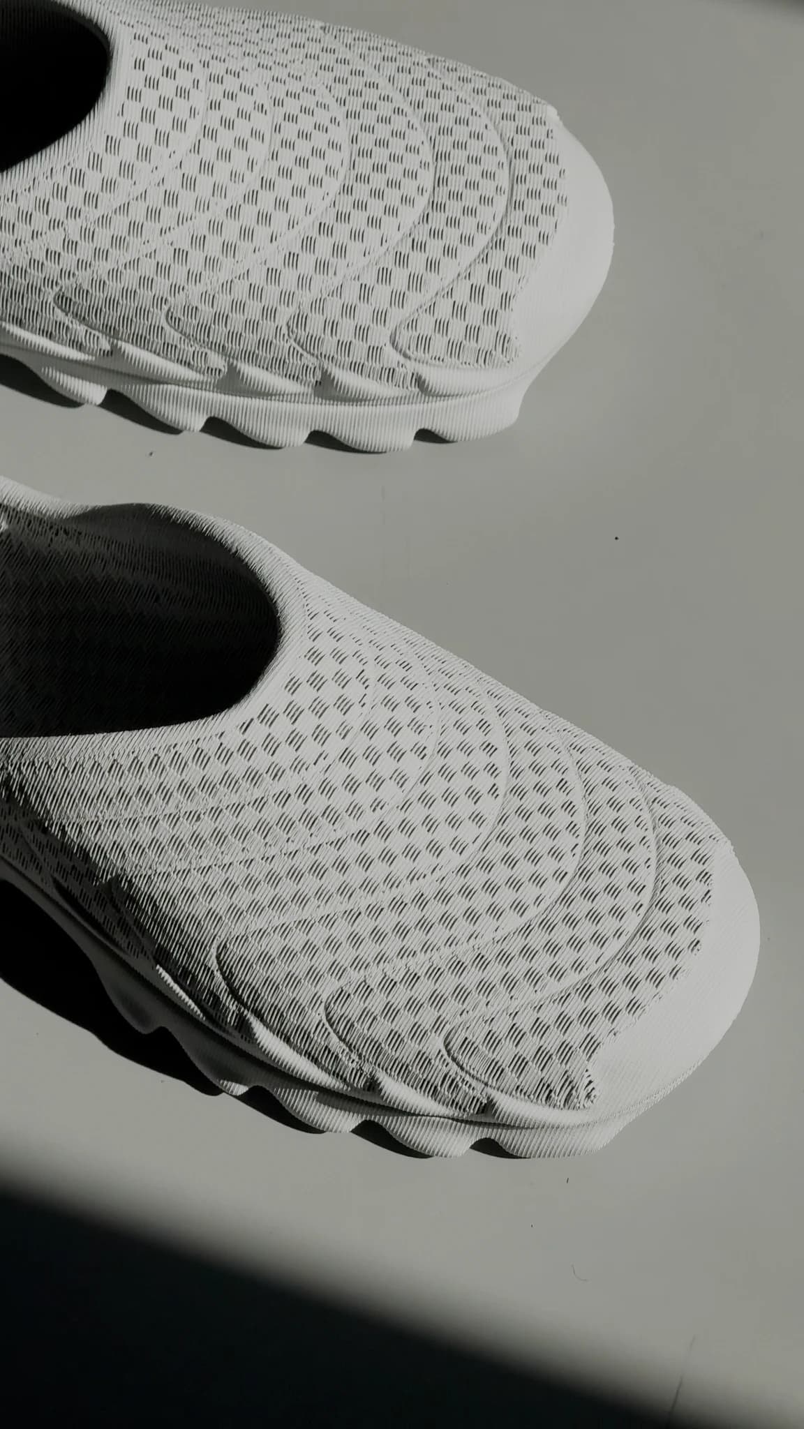 The white VIZE pair standing on a white floor in direct sunlight, one shoe close to the camera, the perforated upper and lugged sole both catching hard light