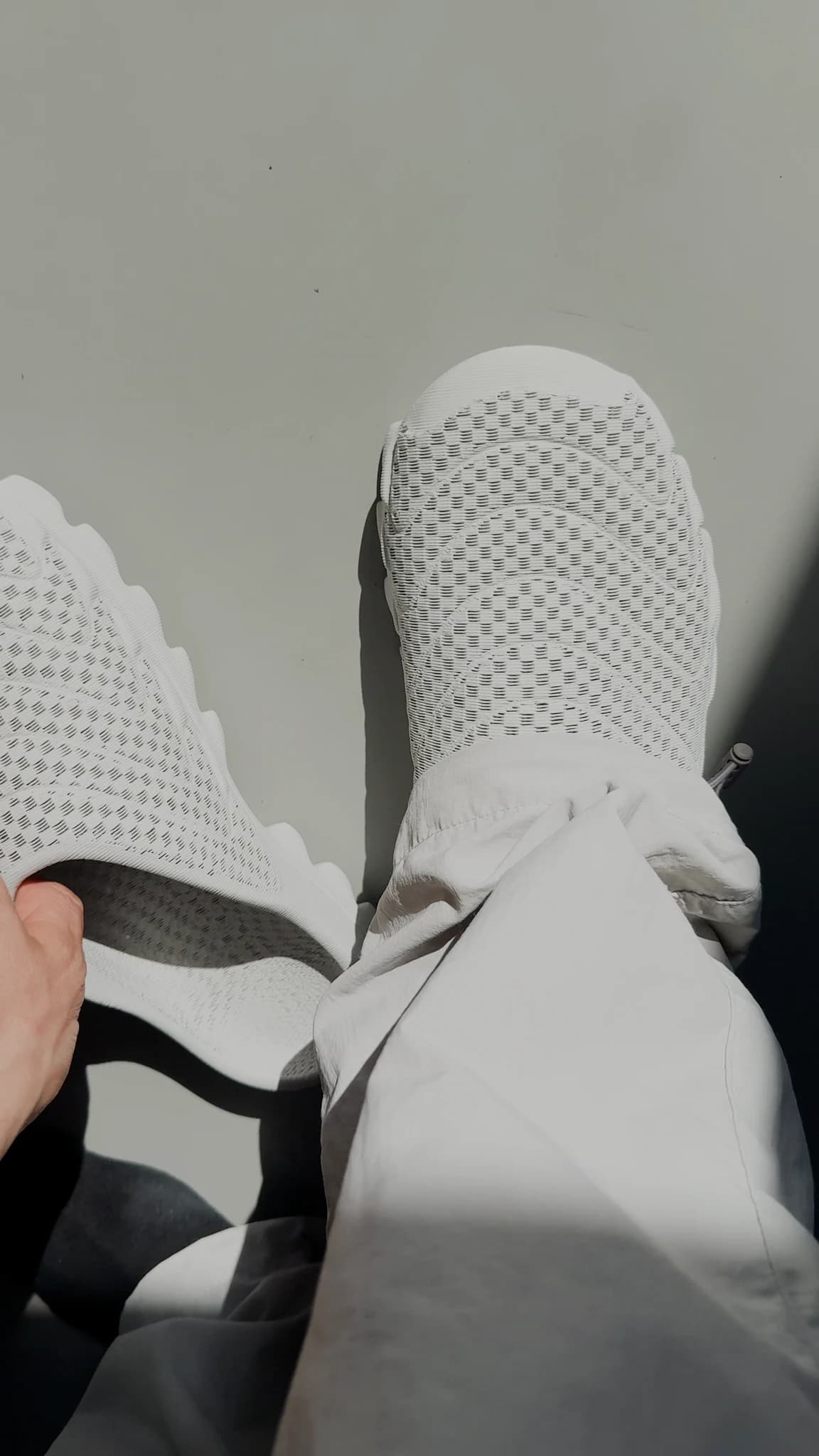A leg raised toward the camera in white trousers, the shoe filling the top of the frame in strong sunlight