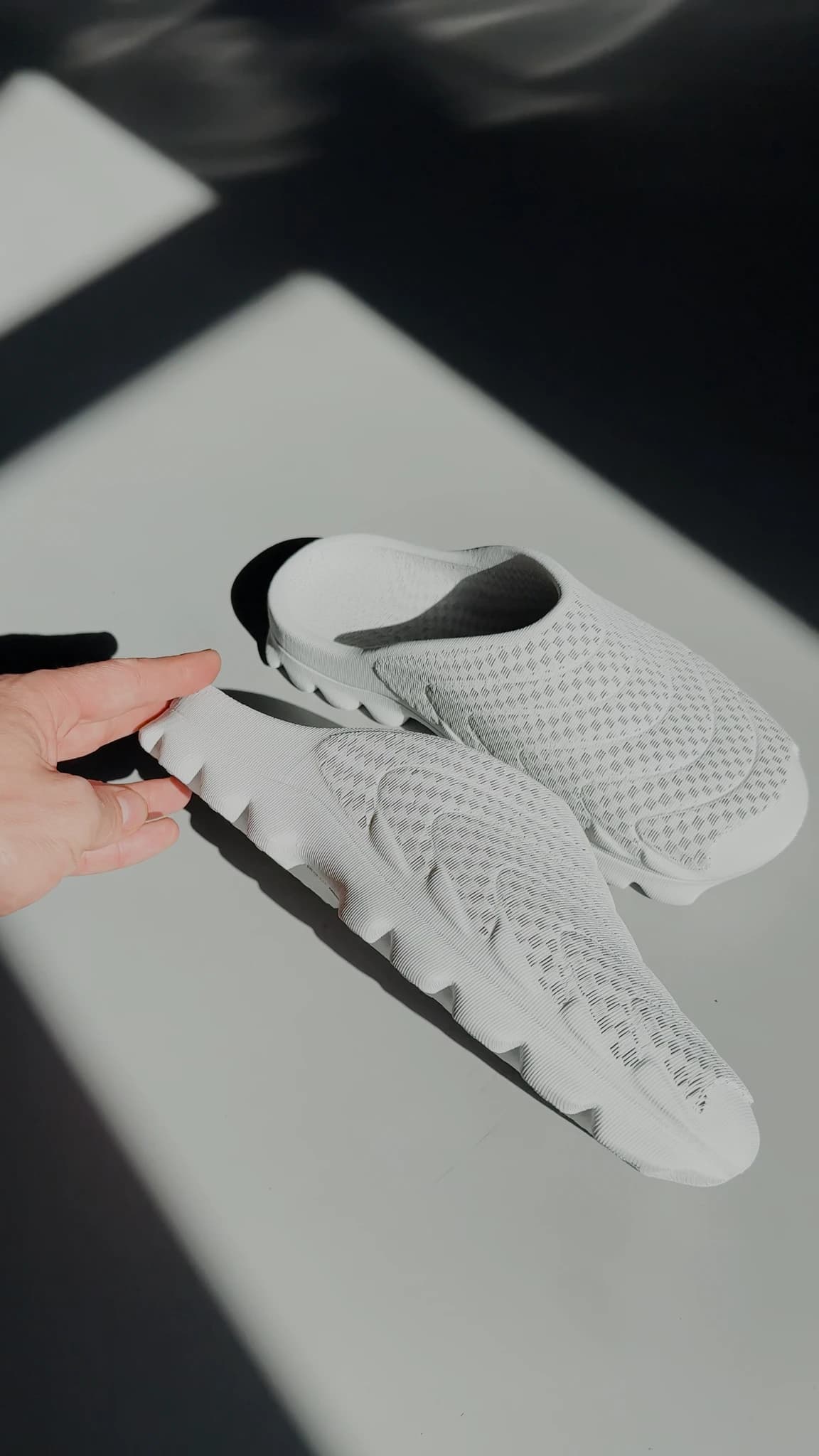 A hand tipping the shoe over on a bright white surface to show the deep lugged outsole