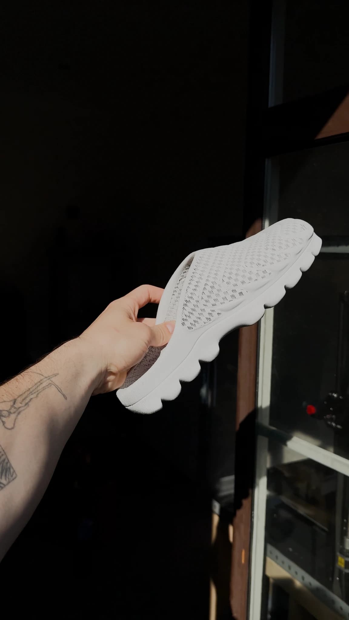 The shoe held up sole-outward against a bright window at dusk, the lug pattern reading as a silhouette
