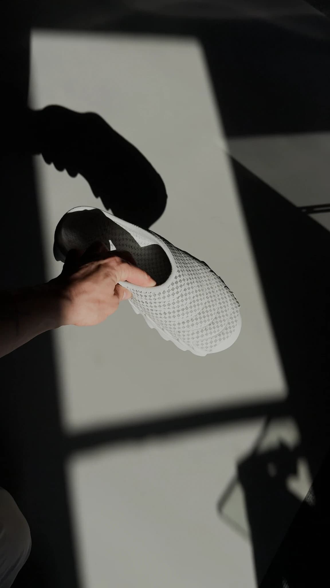 The shoe held above a white surface so it casts a sharp shadow of itself beside it