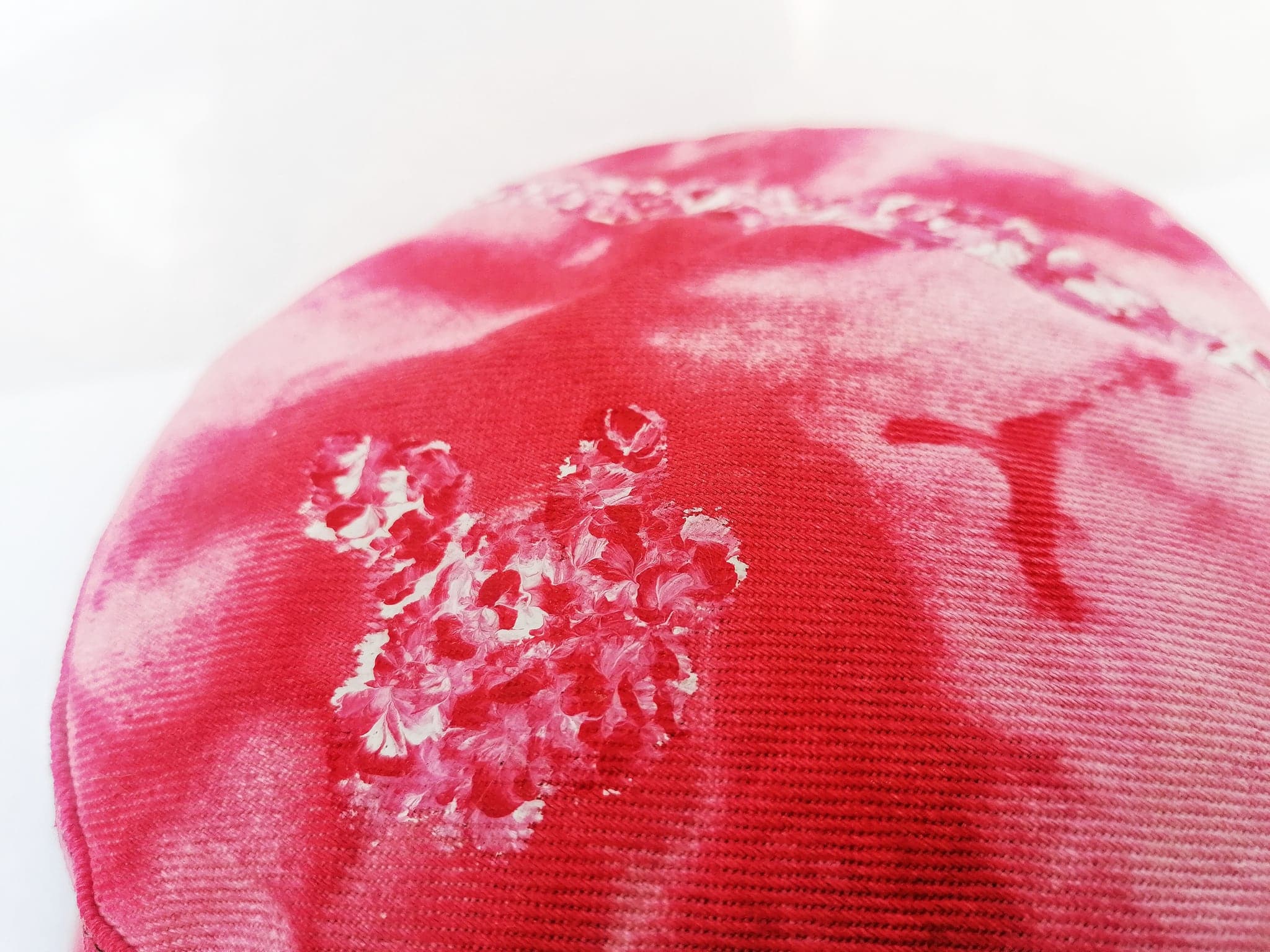A close view of the red hat, the bleached blossom clustered against the stitched rings of the brim