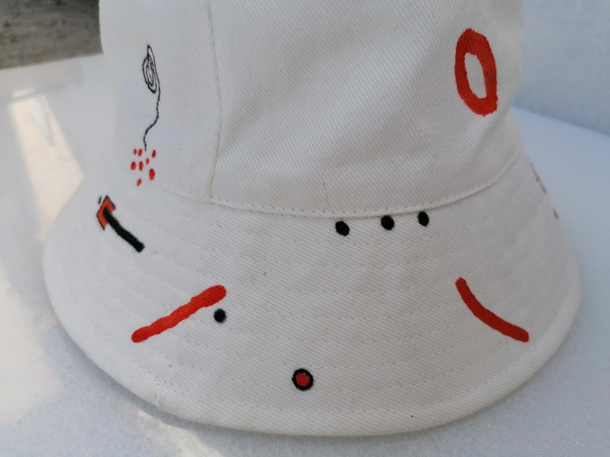 A close view of the white hat, two red ovals, a black stroke and three dots placed far apart