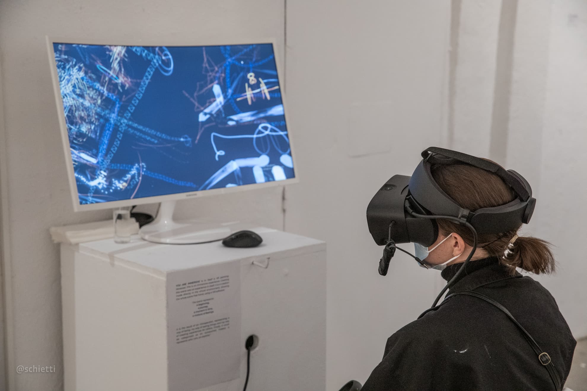 The viewing station at the exhibition, a monitor showing the blue wireframe world and one visitor in a headset beside it