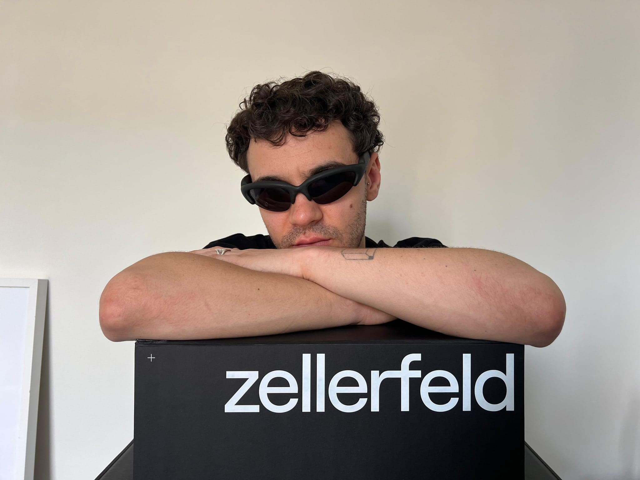 Leaning on a Zellerfeld box, wearing dark frames